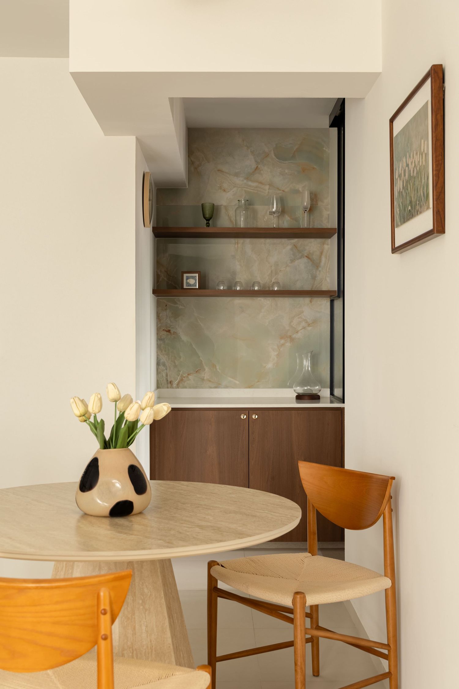 Modern dining nook with round wood table, tulip vase, mid-century chairs, and built-in bar cabinet with marble backsplash.