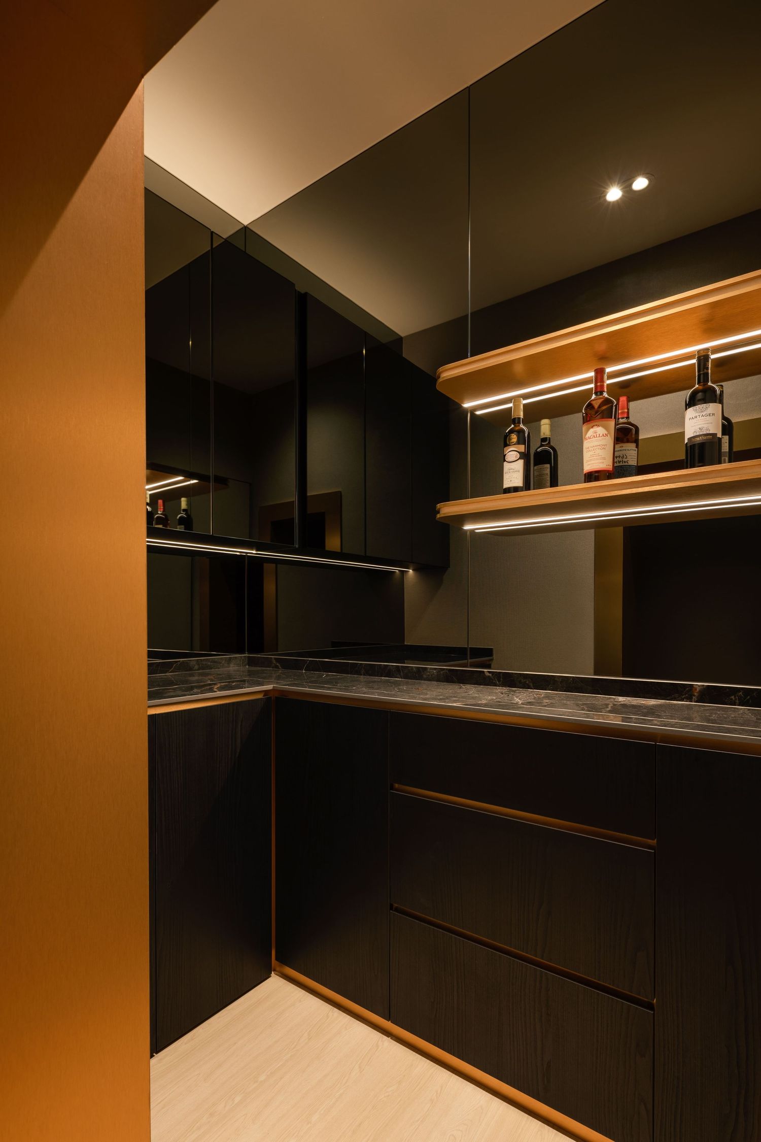 Sleek dark kitchen bar with black cabinetry, marble countertop, warm LED lighting, and wine bottles displayed on a wooden shelf.