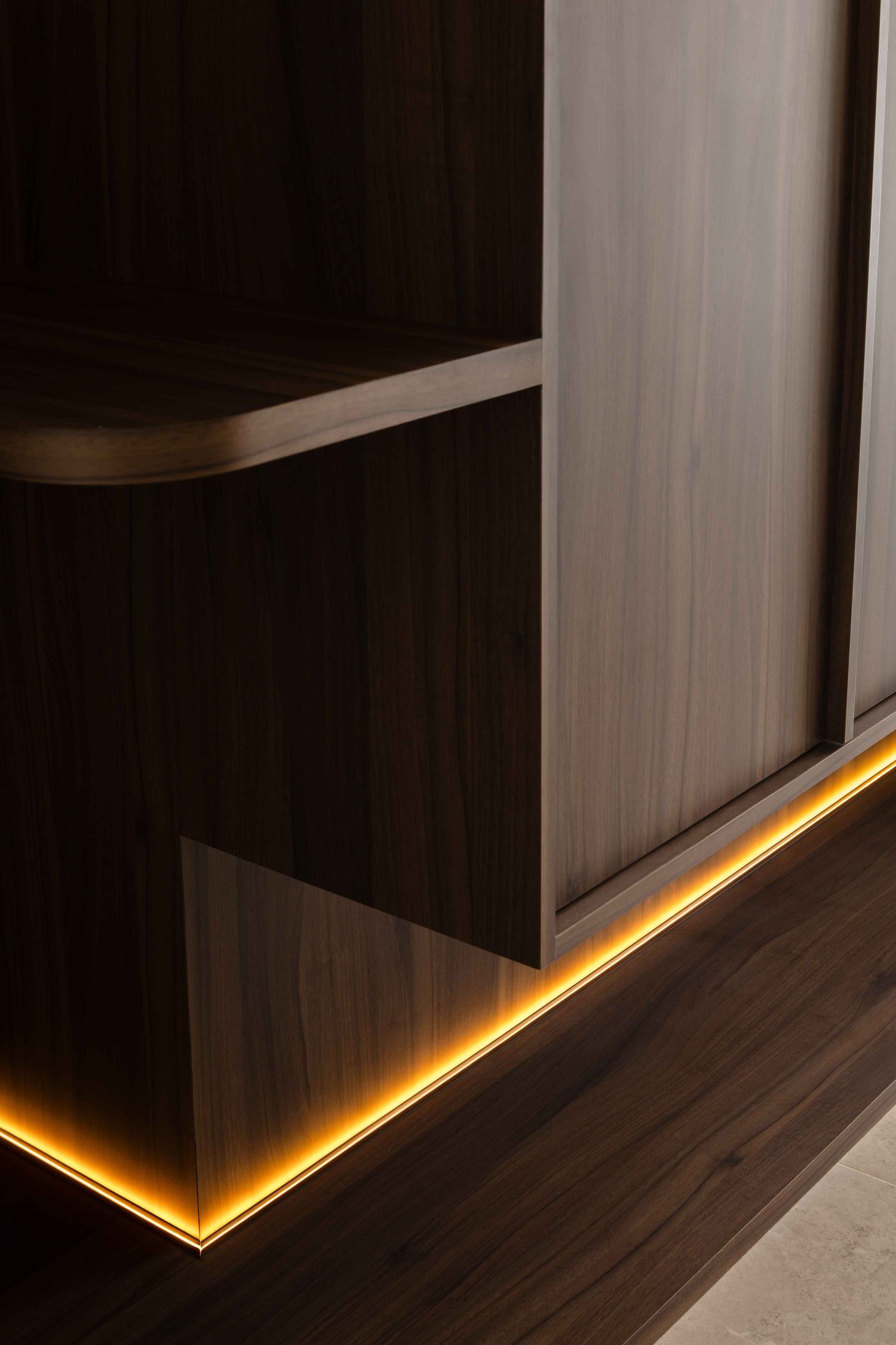 Modern interior design featuring LED strip lighting under dark cabinets creating a warm ambient glow along wooden flooring.