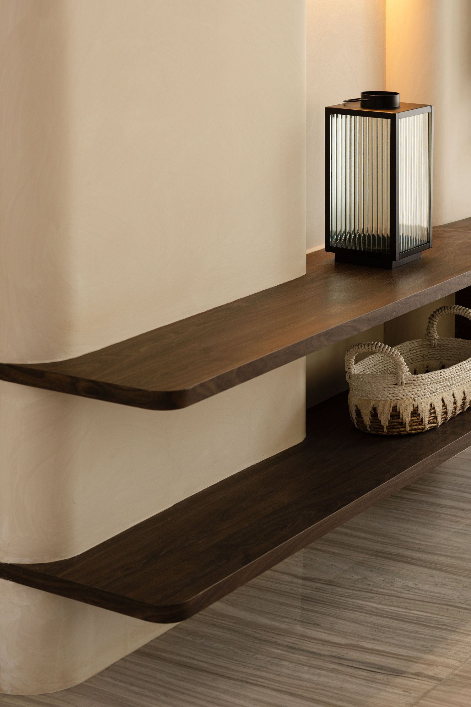 Modern floating wooden shelves with dark stain mounted on white wall displaying lantern and woven basket decor.