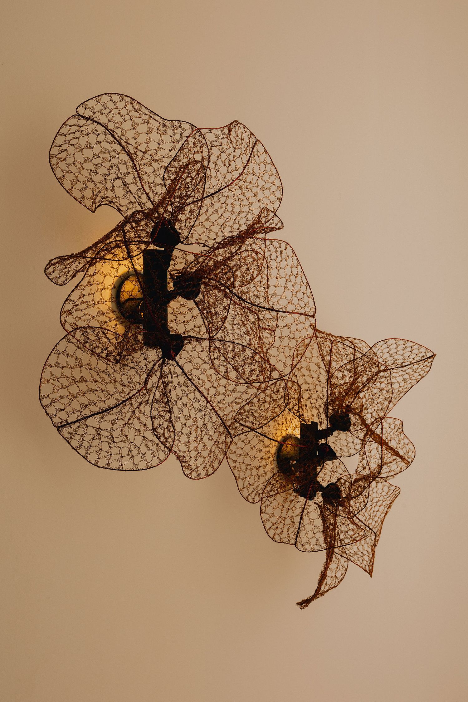 Artistic wall sconce with intricate lace-like leaf design and warm glowing lights on beige wall.
