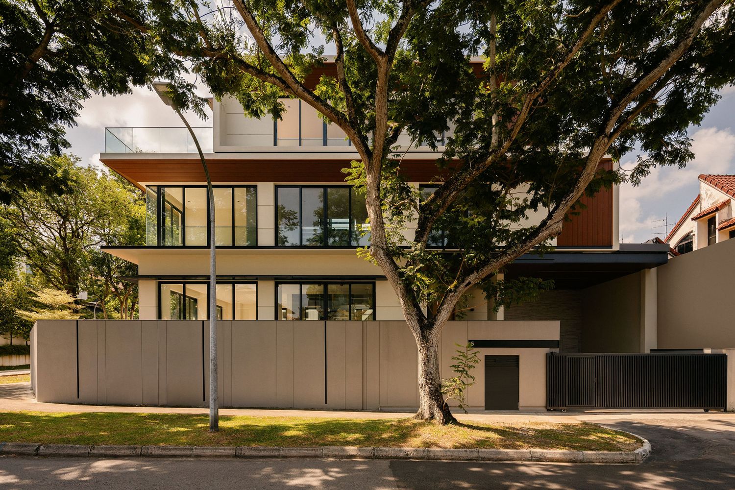 Modern multi-story residential building with floor-to-ceiling glass windows, timber accents, and a gated entrance shaded by mature trees.