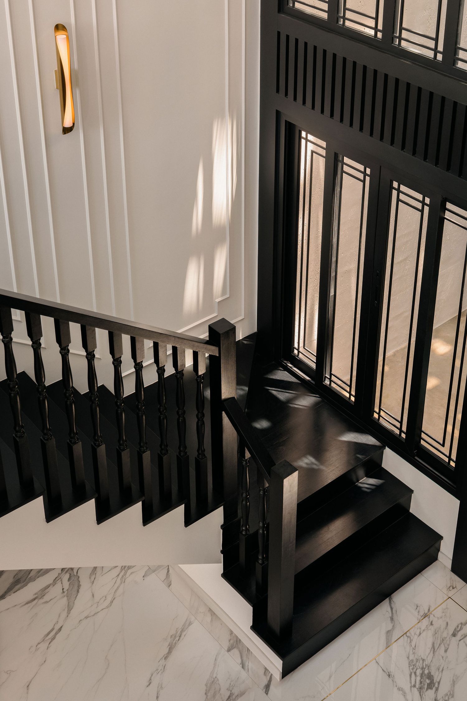 Black wooden staircase with spindle balustrade and glass panel screen beside white paneled walls and a marble floor in a modern home.