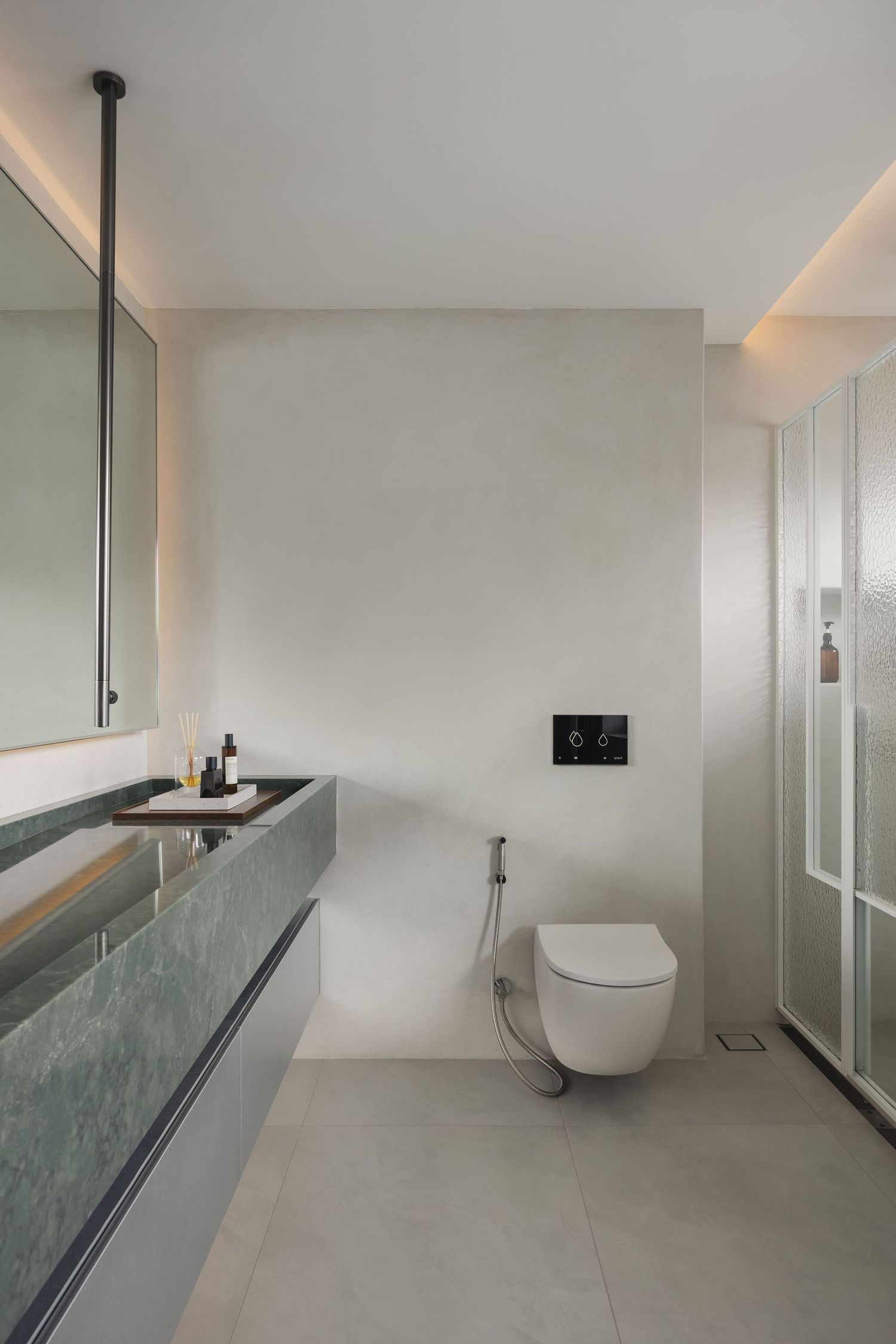 Modern minimalist bathroom with wall-mounted toilet, green marble vanity, large mirror, and glass shower enclosure.