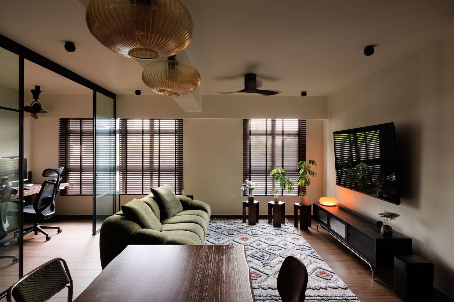 Modern living room with green sofa, patterned rug, wall-mounted TV, wooden furniture, and woven pendant lights.
