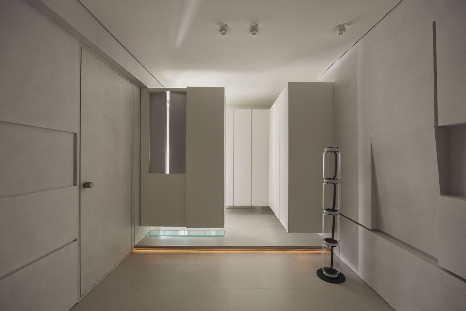 Minimalist modern interior hallway with white walls, recessed lighting, and sleek gray panels in a contemporary space.