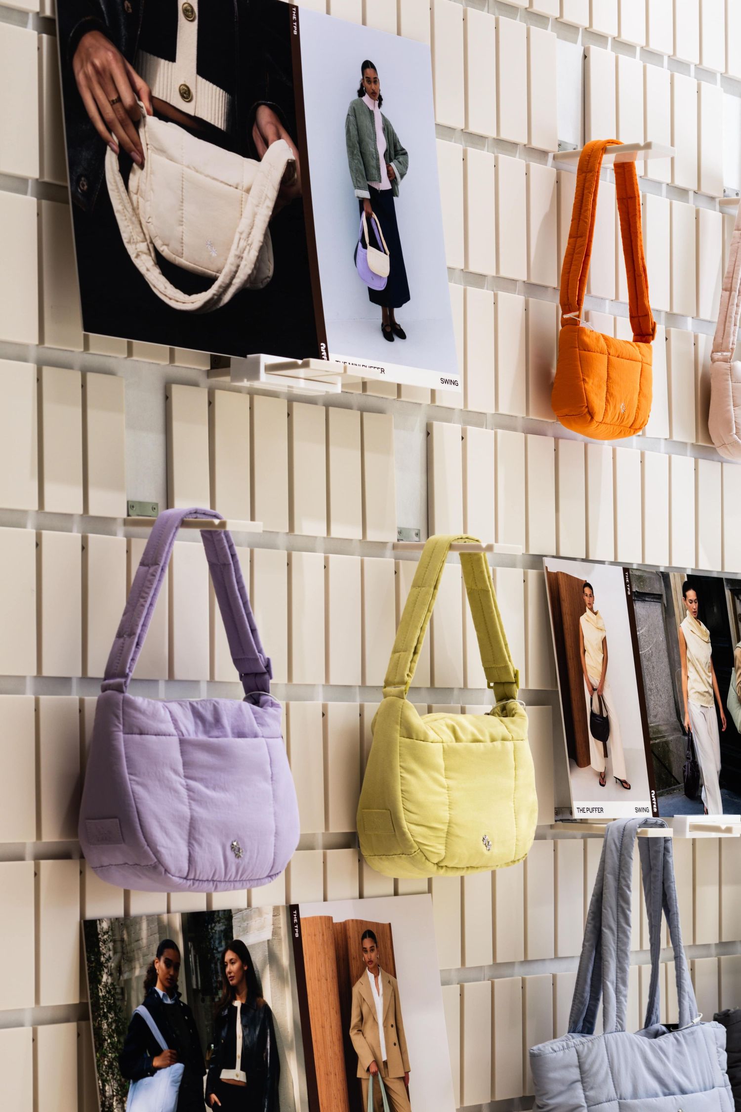 A display wall featuring colorful fabric tote bags in pastel shades with fashion photography mounted between them.