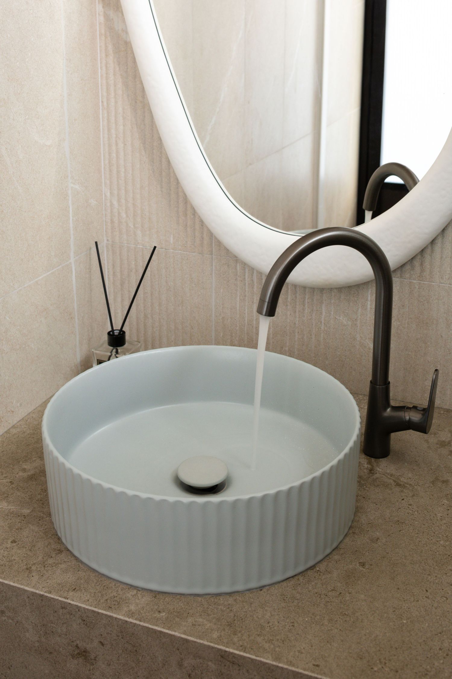 Modern white circular vessel sink with ribbed texture and matte black faucet in contemporary bathroom design.