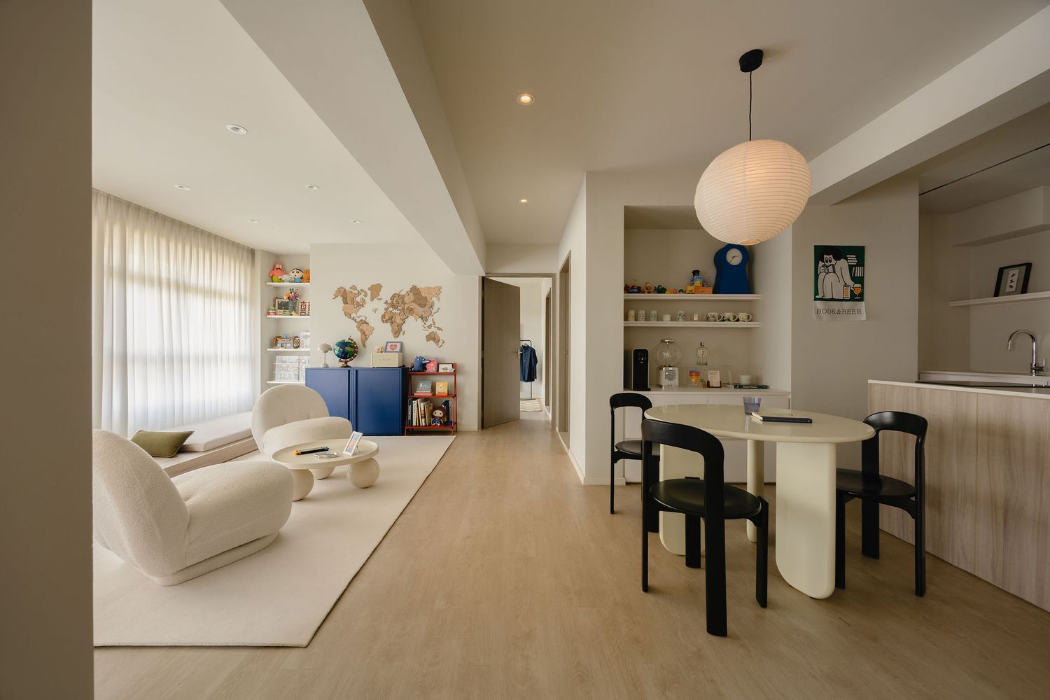 Modern open-plan living and dining room with white furniture, black chairs, pendant light, and light wood flooring.