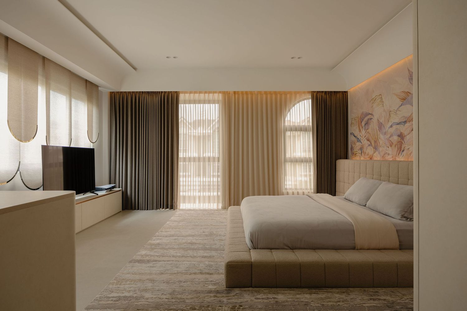 Modern luxury bedroom with beige tones, arched windows, plush bed, TV console, and elegant curtains in a minimalist design.