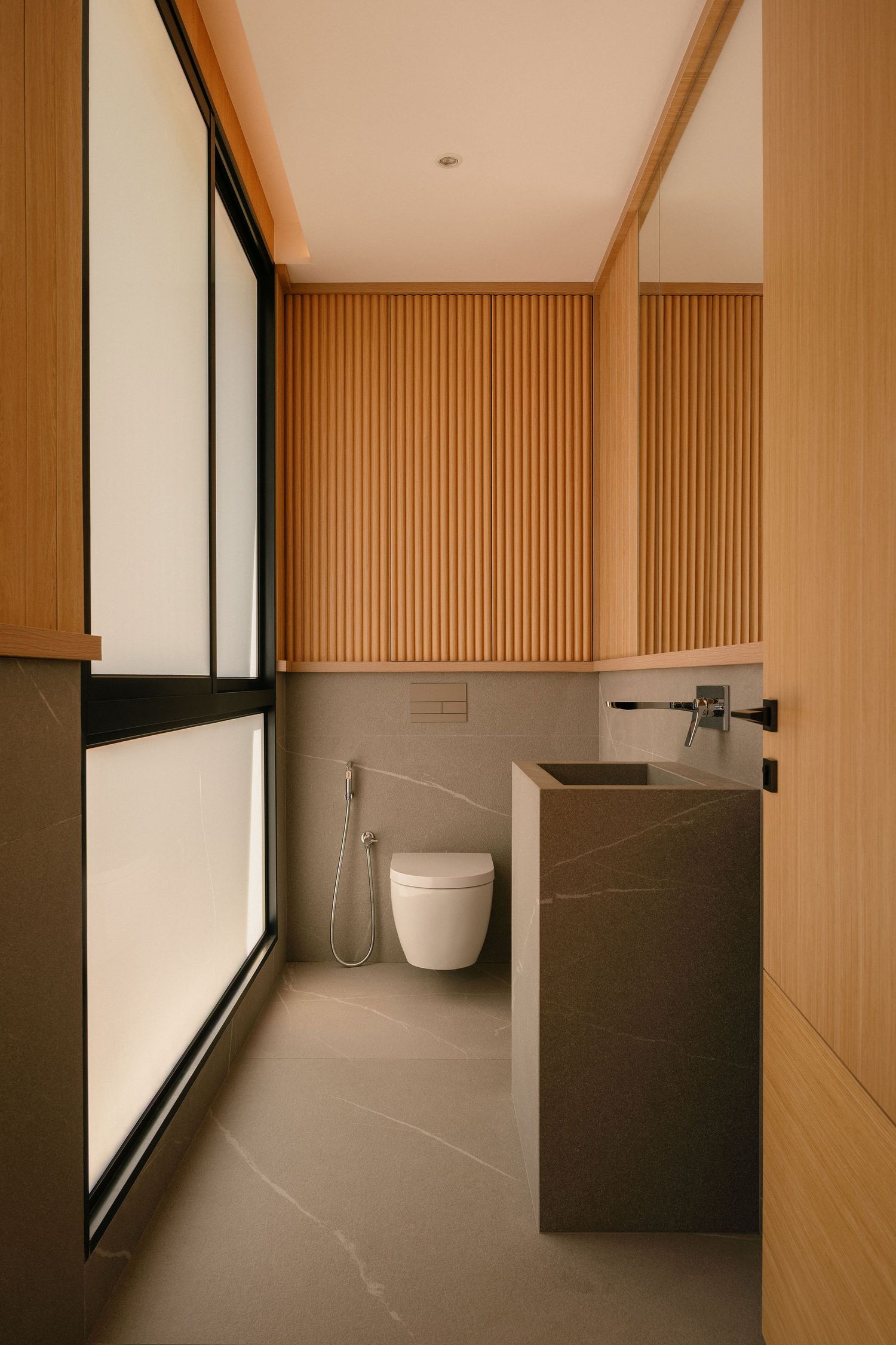 Modern minimalist bathroom with wood slat walls, a stone vanity sink, wall-mounted toilet with bidet spray and frosted glass windows.
