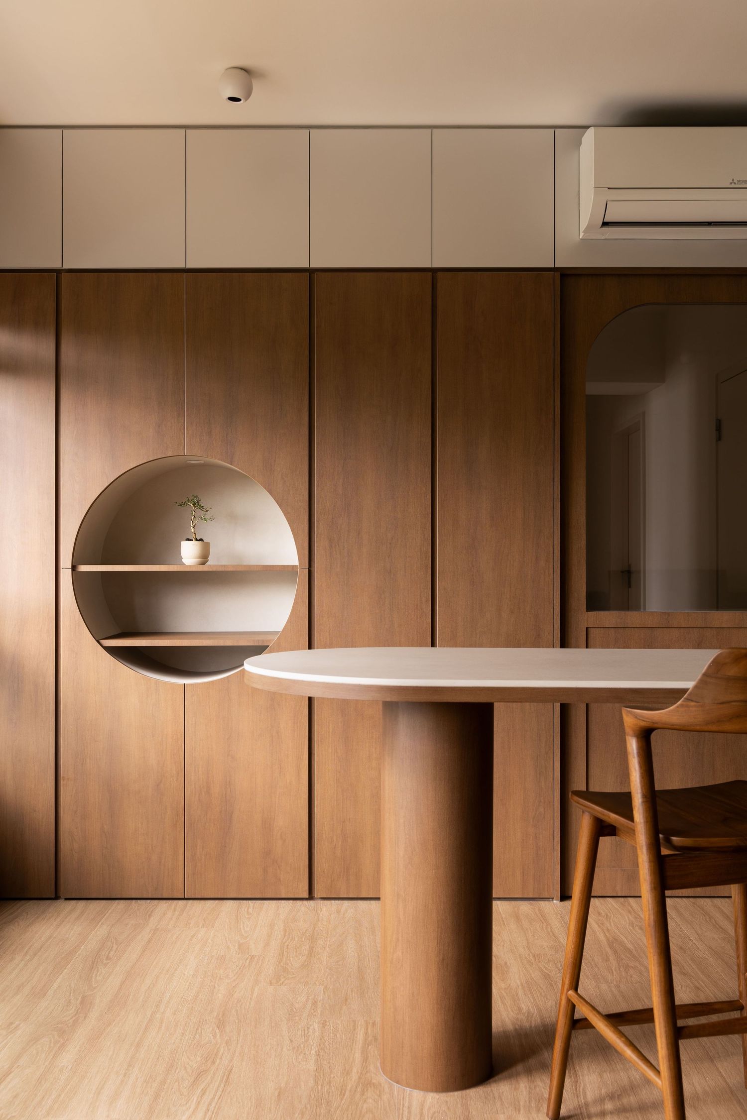 Modern minimalist interior with wooden wall panels, circular shelf niche, and cylindrical pedestal table with bar stool.