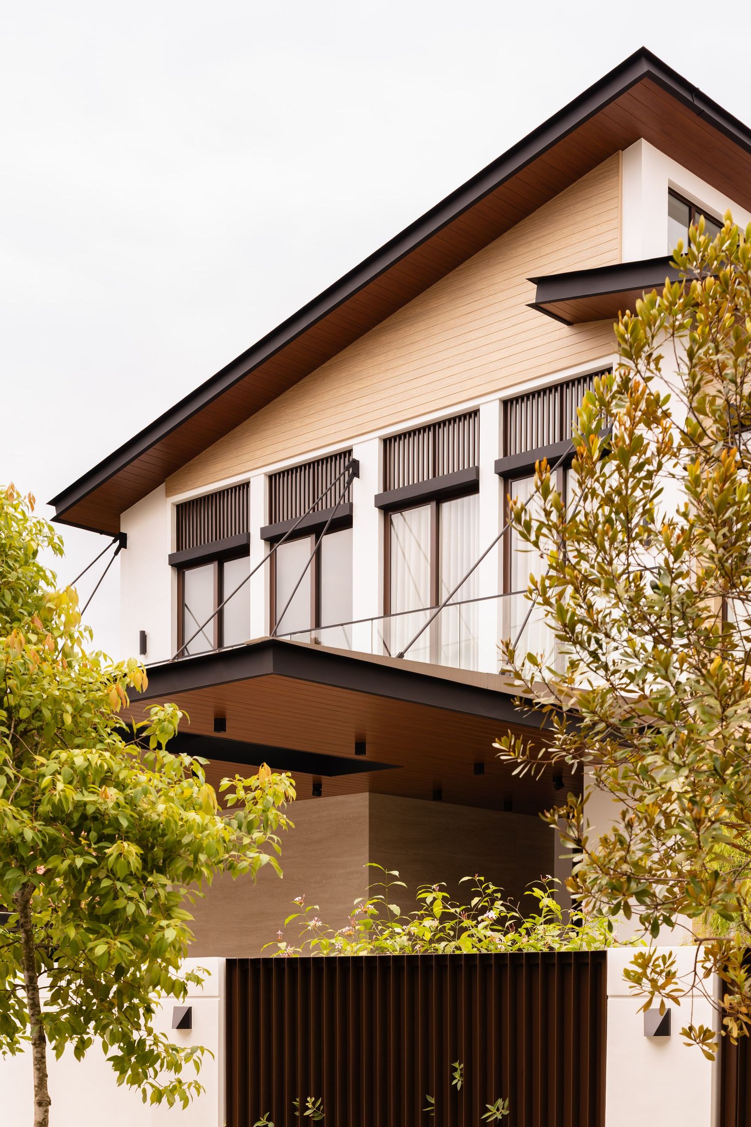 Modern two-story house exterior with brown awnings and cream-colored siding surrounded by autumn trees.