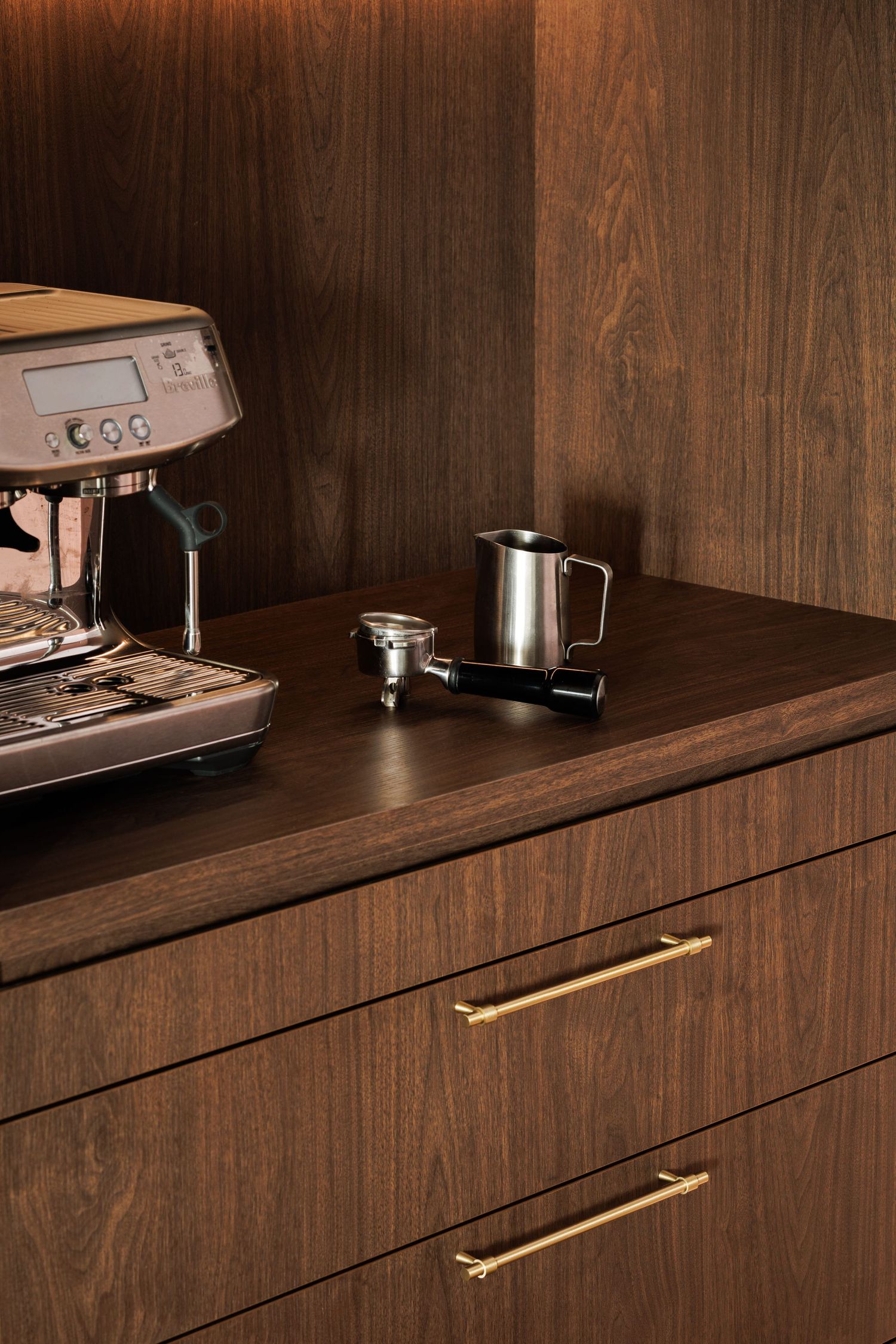 Modern dark wood kitchen cabinets with sleek brass handles and built-in appliances on a wooden countertop.