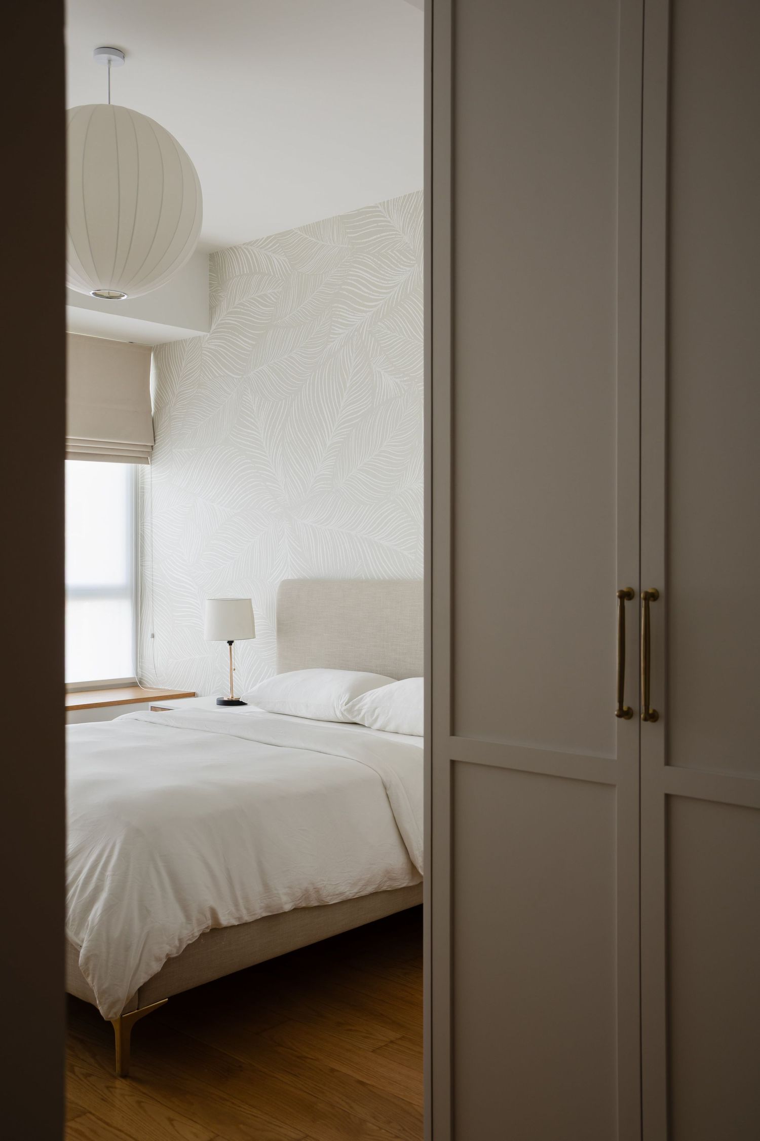 Minimalist bedroom interior with white bedding, wooden floors, and a spherical paper lantern ceiling light.