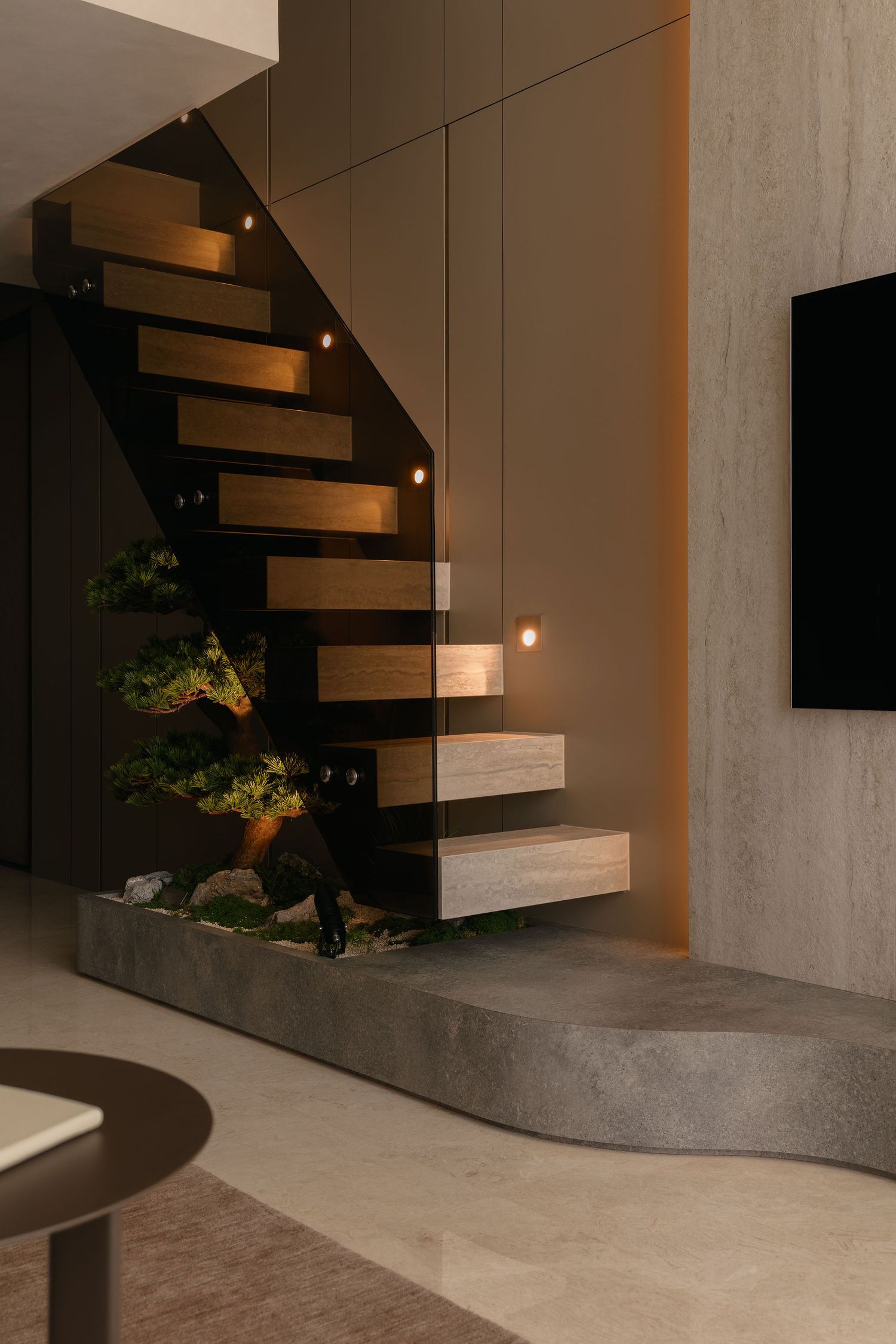 Modern floating wooden staircase with glass railing, LED lights and a bonsai garden on a curved stone base in a contemporary living room.