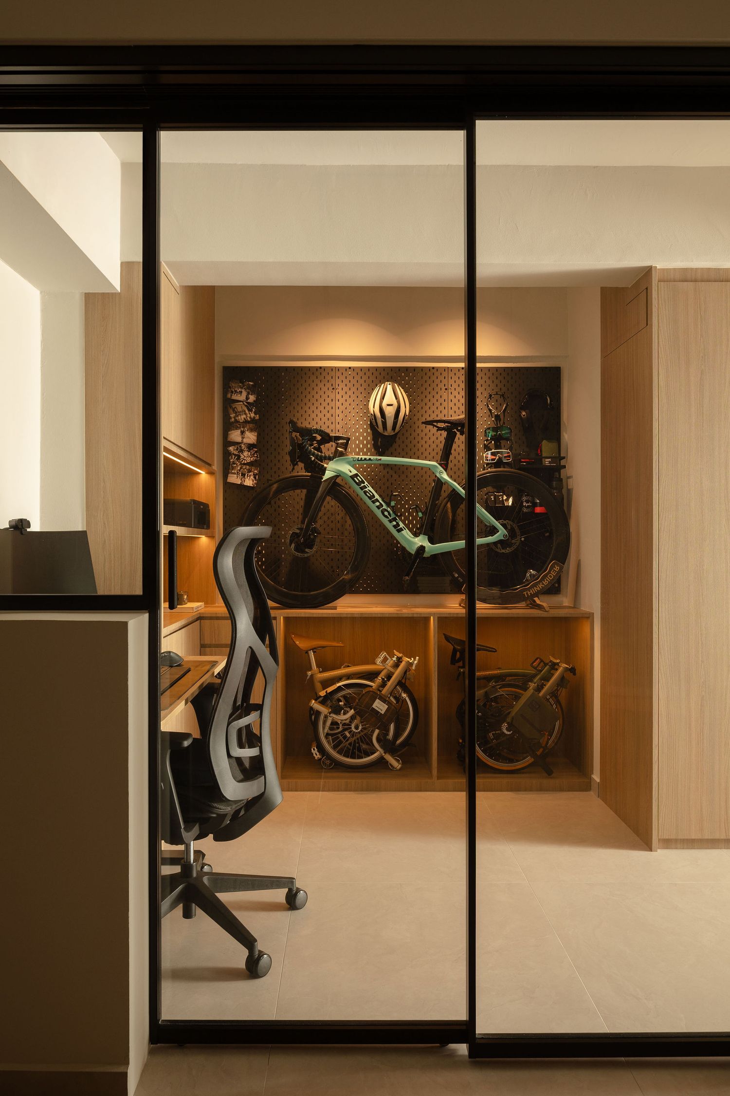 Modern home office with glass partition revealing a bike storage room displaying a Bianchi road bike and Brompton folding bike.