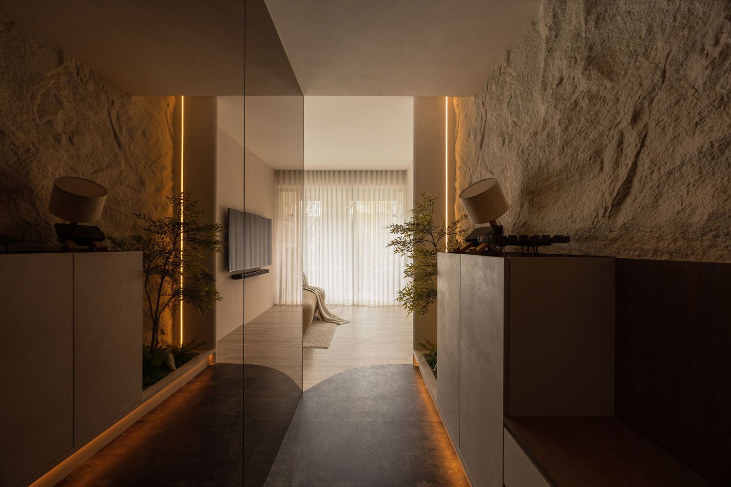 Modern interior hallway with warm LED lighting, natural stone walls, and a view into a bright living space.