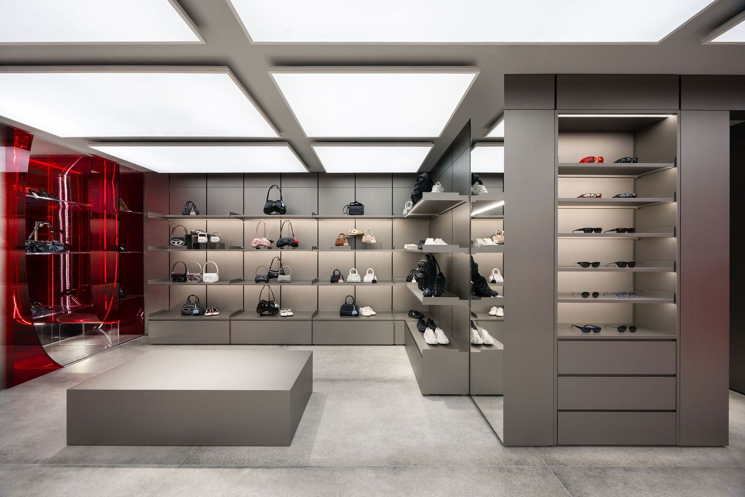 Modern luxury retail store interior with gray shelving displaying handbags and shoes, featuring red accent wall display cases.