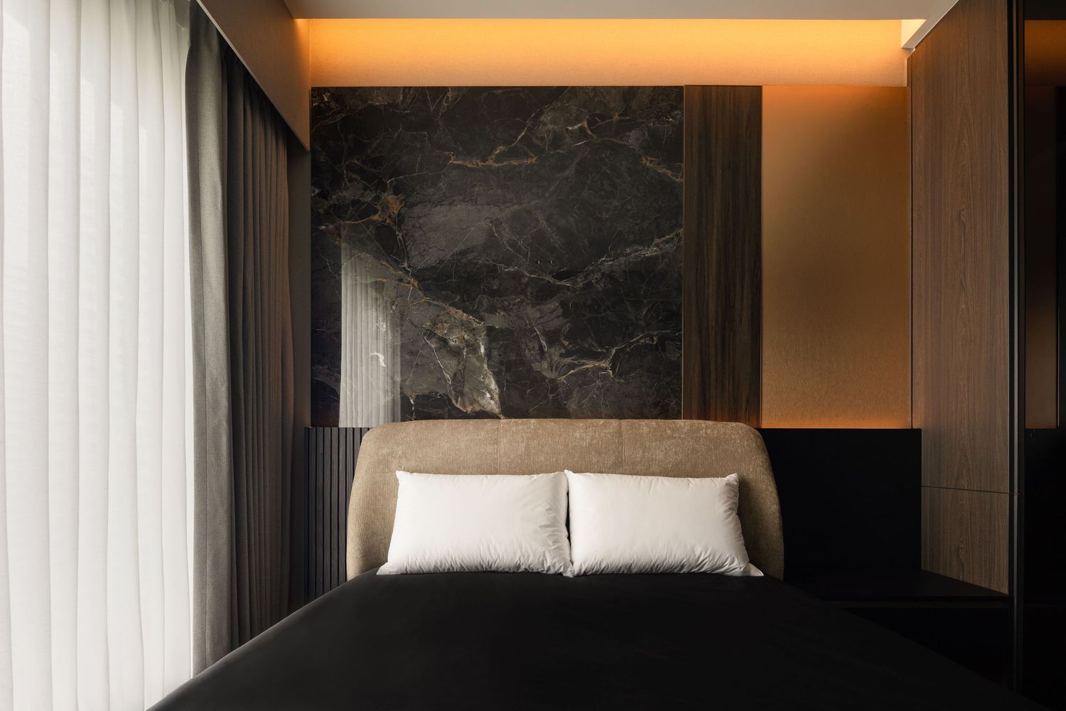 Luxury bedroom with dark marble accent wall, warm ambient lighting, beige upholstered headboard, and black bedding.