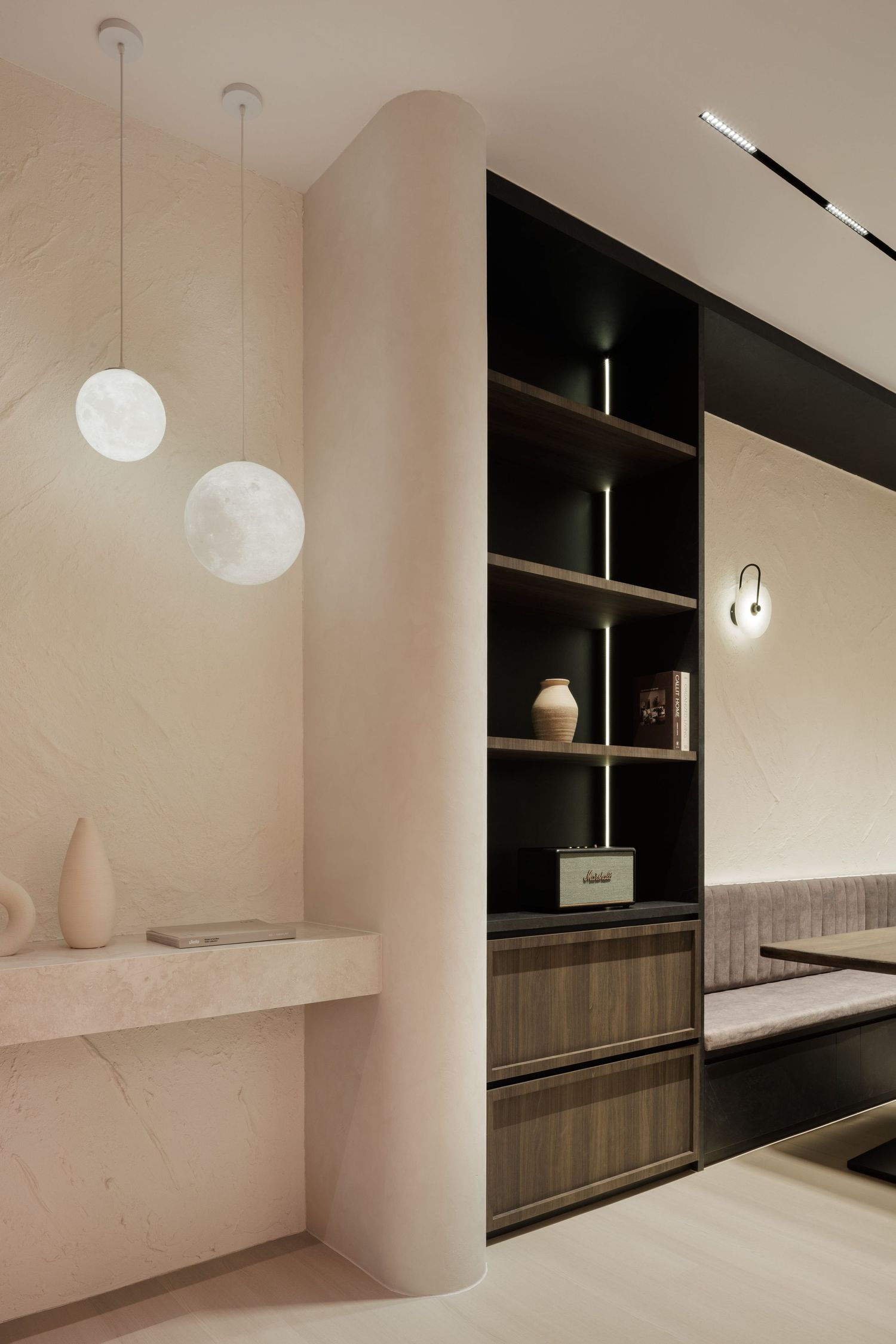 Minimalist interior space with curved walls, pendant lighting, and dark wood built-in shelving against white walls.