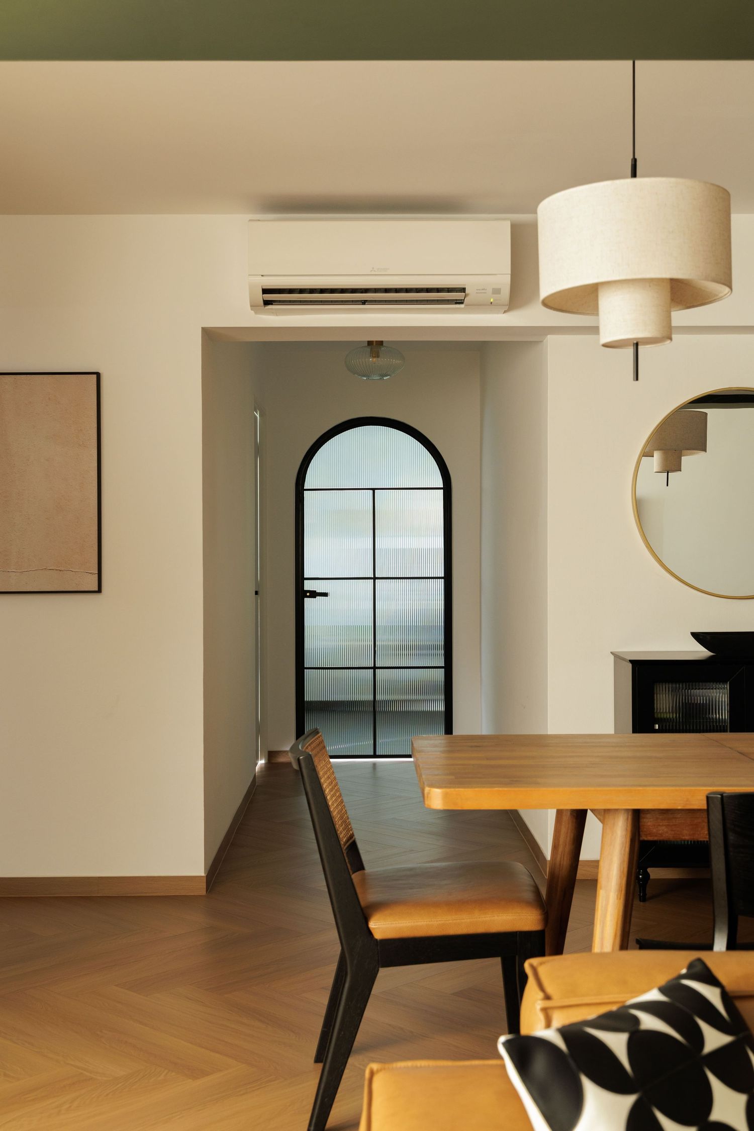 Modern minimalist dining area with herringbone wood flooring, black chairs, and an arched window letting in natural light.