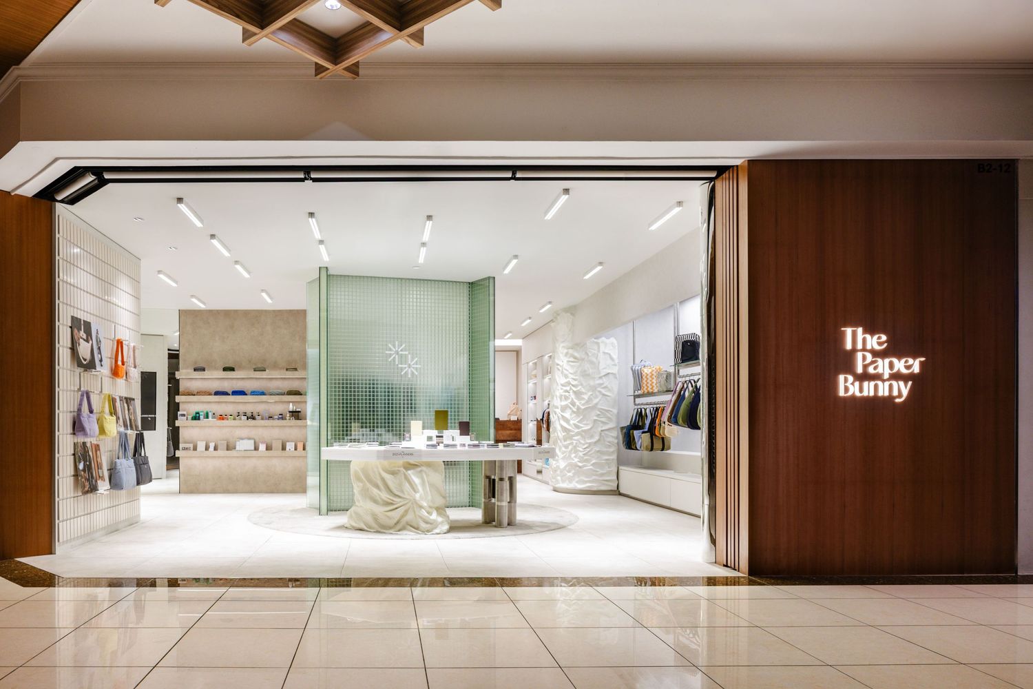 Modern storefront of The Paper Store featuring bright white interior, glass displays and wood accented entrance in a mall setting.