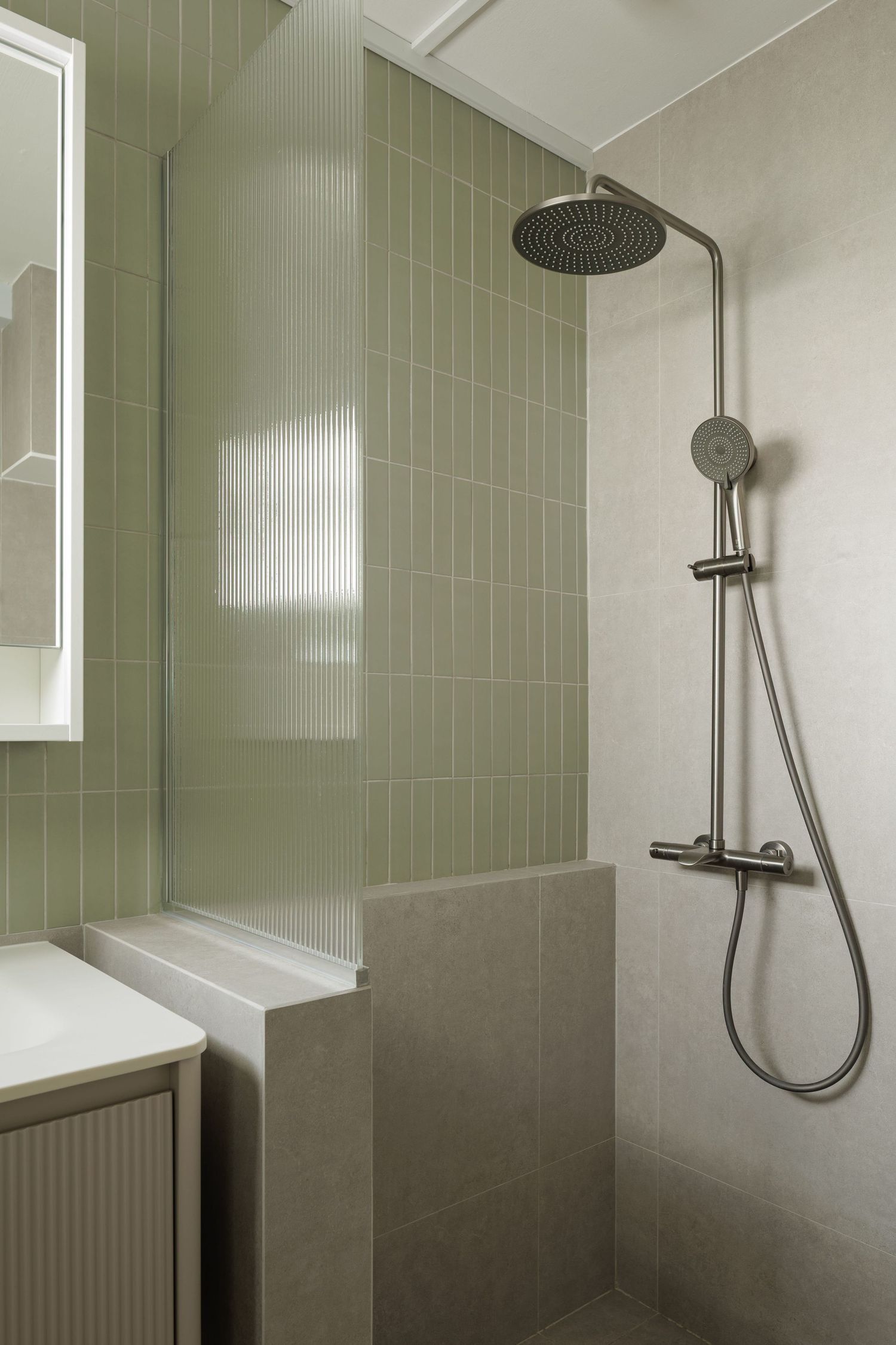 Modern bathroom with sage green tile walls, rain shower head, and minimalist fixtures in a sleek design.