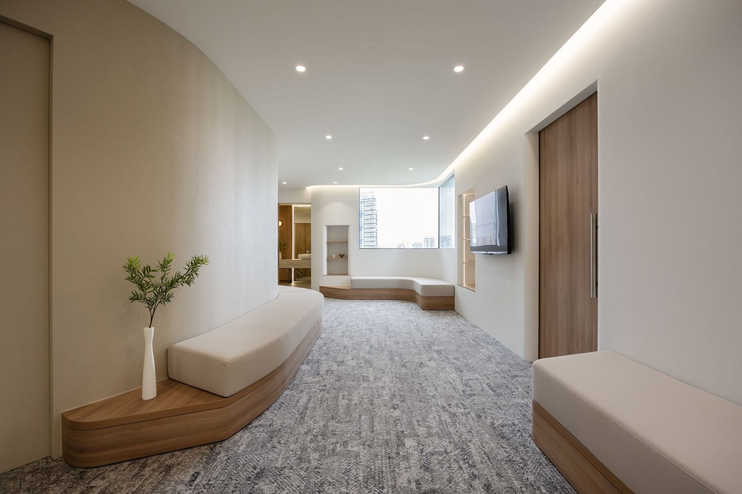 Modern minimalist bedroom interior with grey carpet flooring, white walls and built-in wooden storage features.