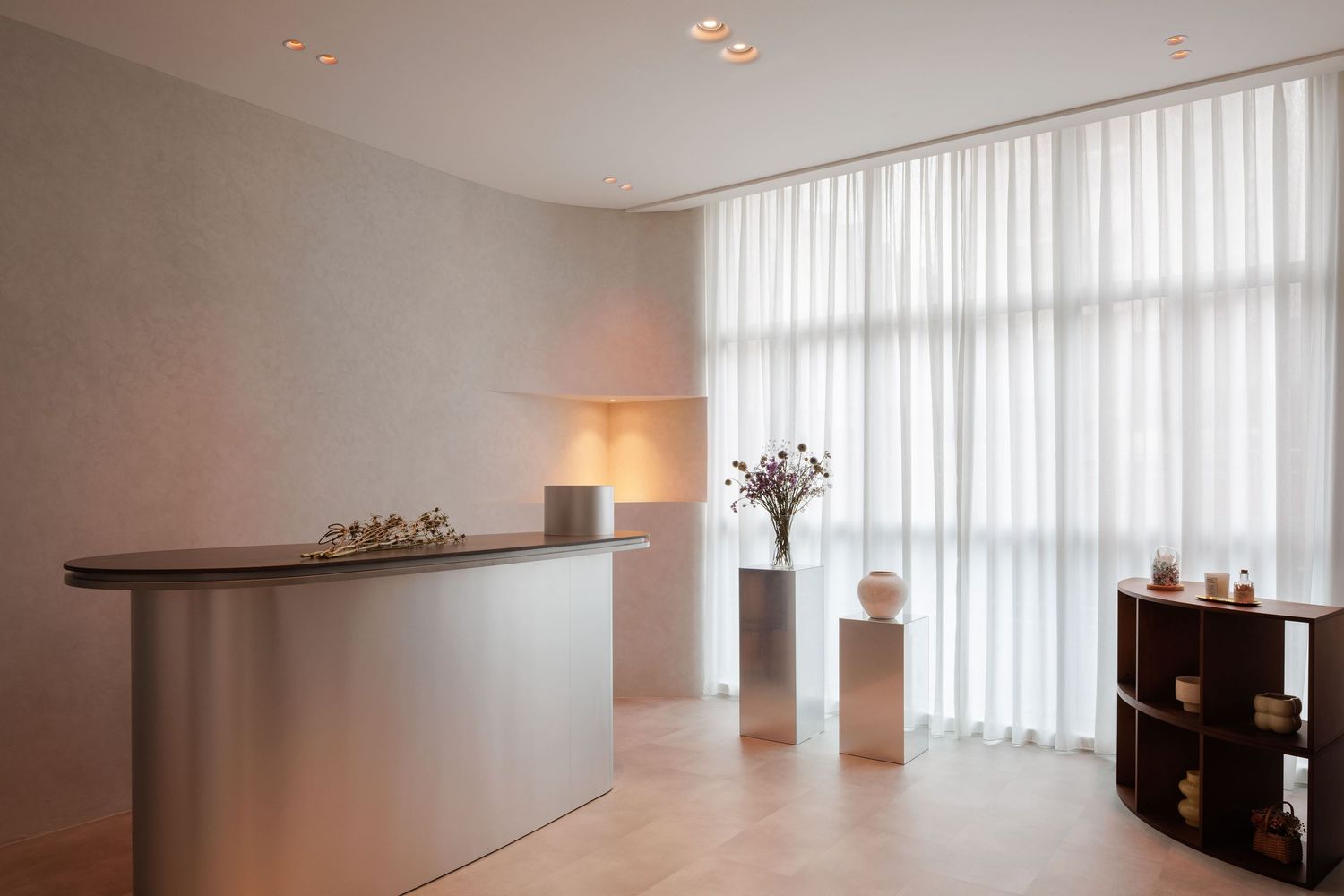 Modern minimalist reception area with white walls, floor-length sheer curtains, and decorative vases on pedestals.