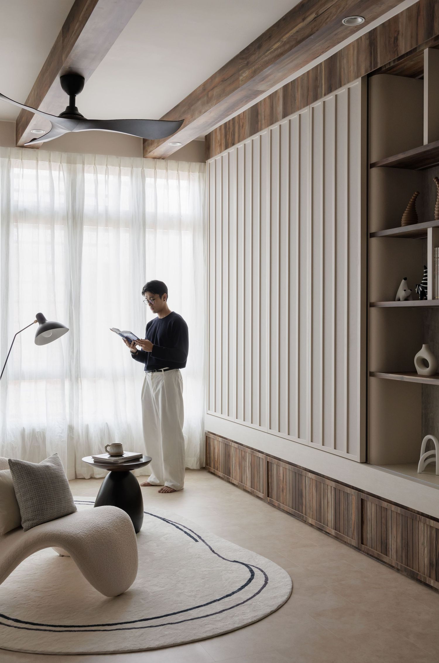 Modern minimalist living room with vertical white paneling, built-in shelves, and curved accent chair on a circular rug.