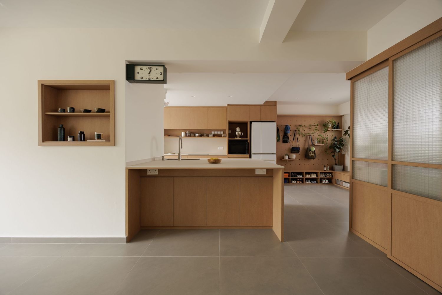 Modern minimalist kitchen with wooden cabinets, white countertops, and built-in shelving in a neutral-toned interior space.