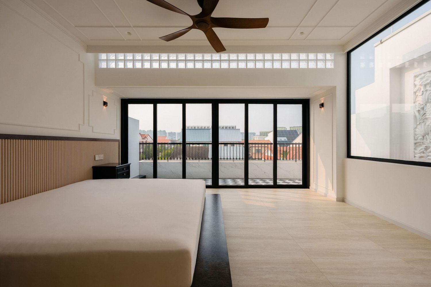 Bright modern bedroom with a low platform bed, ceiling fan, wood floors, and black-framed glass doors opening to a sunny balcony.