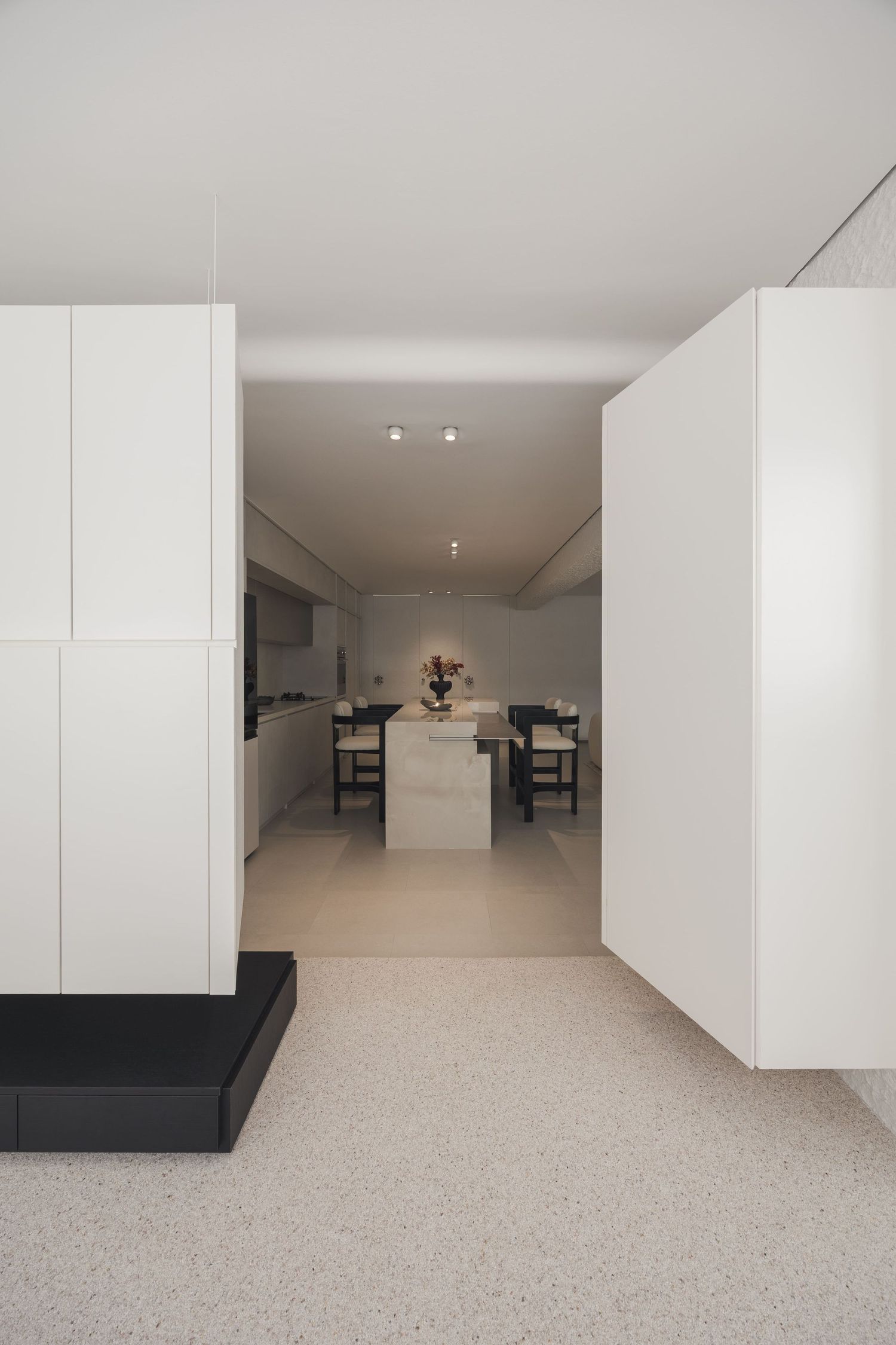 Minimalist white kitchen with marble island, terrazzo floors, and sleek cabinetry in a modern open-plan interior.