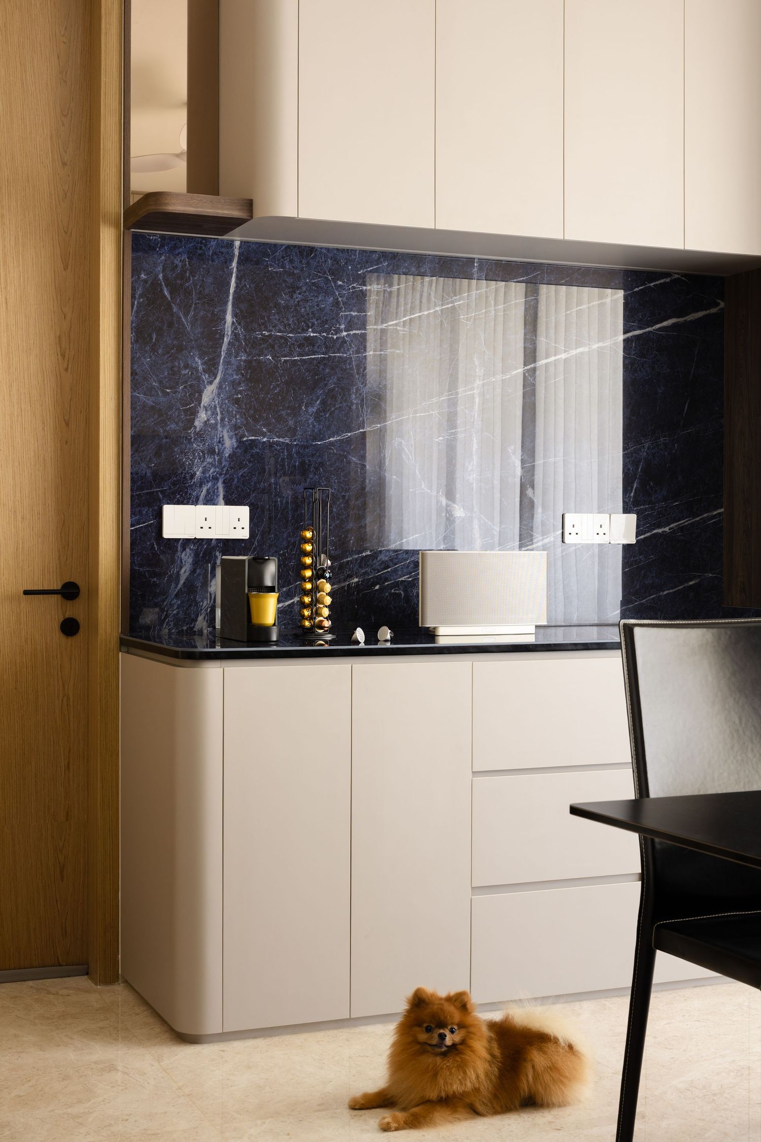 Modern kitchen interior with dark marble backsplash, white cabinets and a small Pomeranian dog resting on the floor.