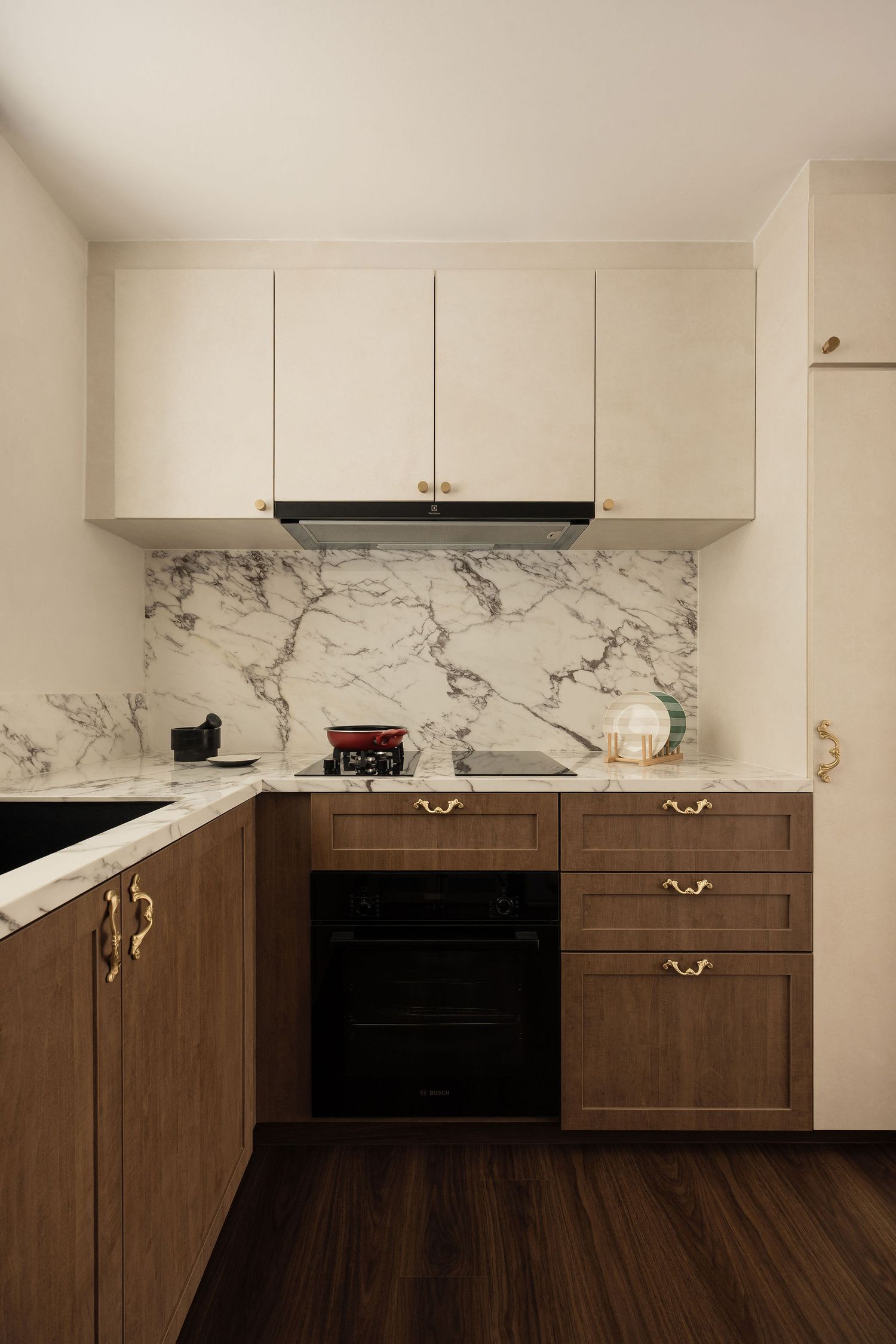 Modern kitchen with marble backsplash, dark wood lower cabinets, cream upper cabinets, brass hardware, and black built-in oven.