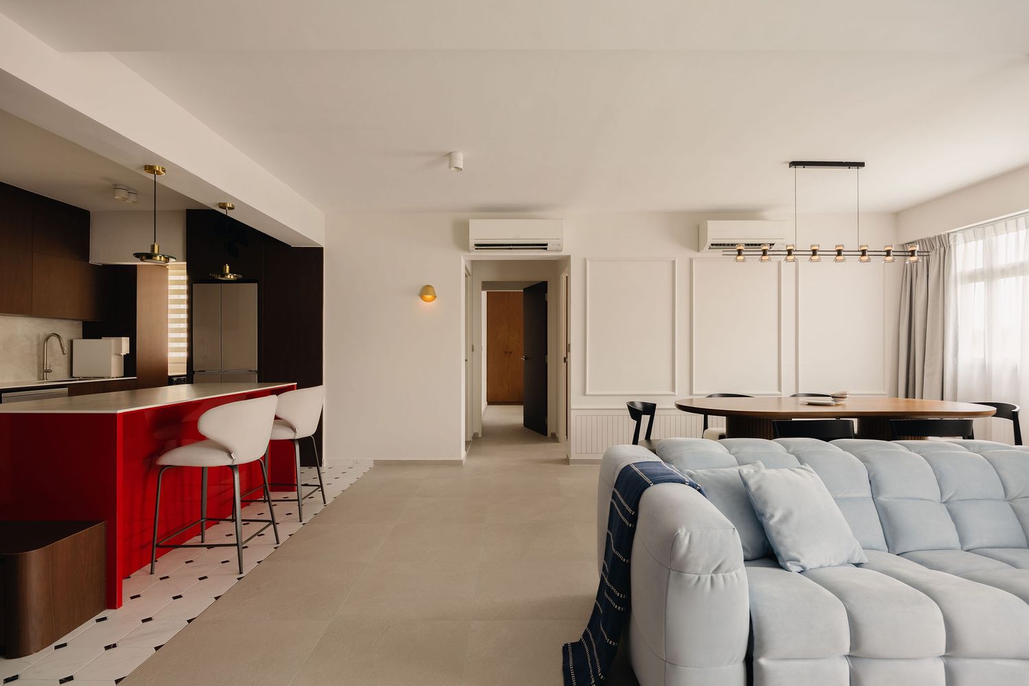 Modern open-plan living space featuring a blue tufted sofa, red kitchen island with bar stools, and dining area with pendant lighting.