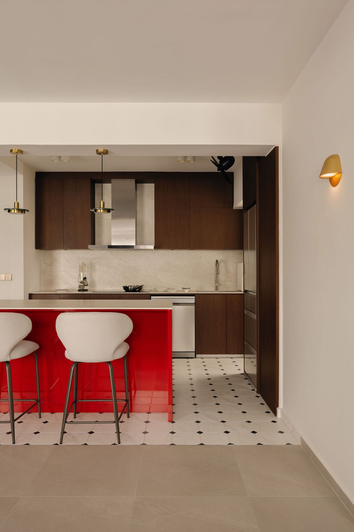Modern kitchen with red island, white bar stools, dark wood cabinets, gold accents, and checkered tile flooring.