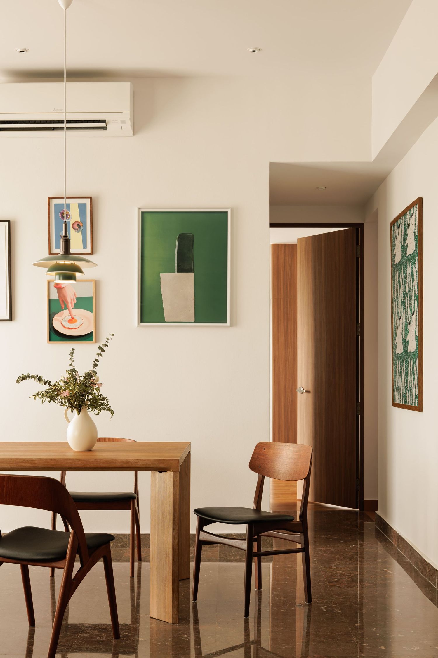 Modern minimalist dining area with wooden chairs, white walls, and green artwork featuring sleek interior design elements.