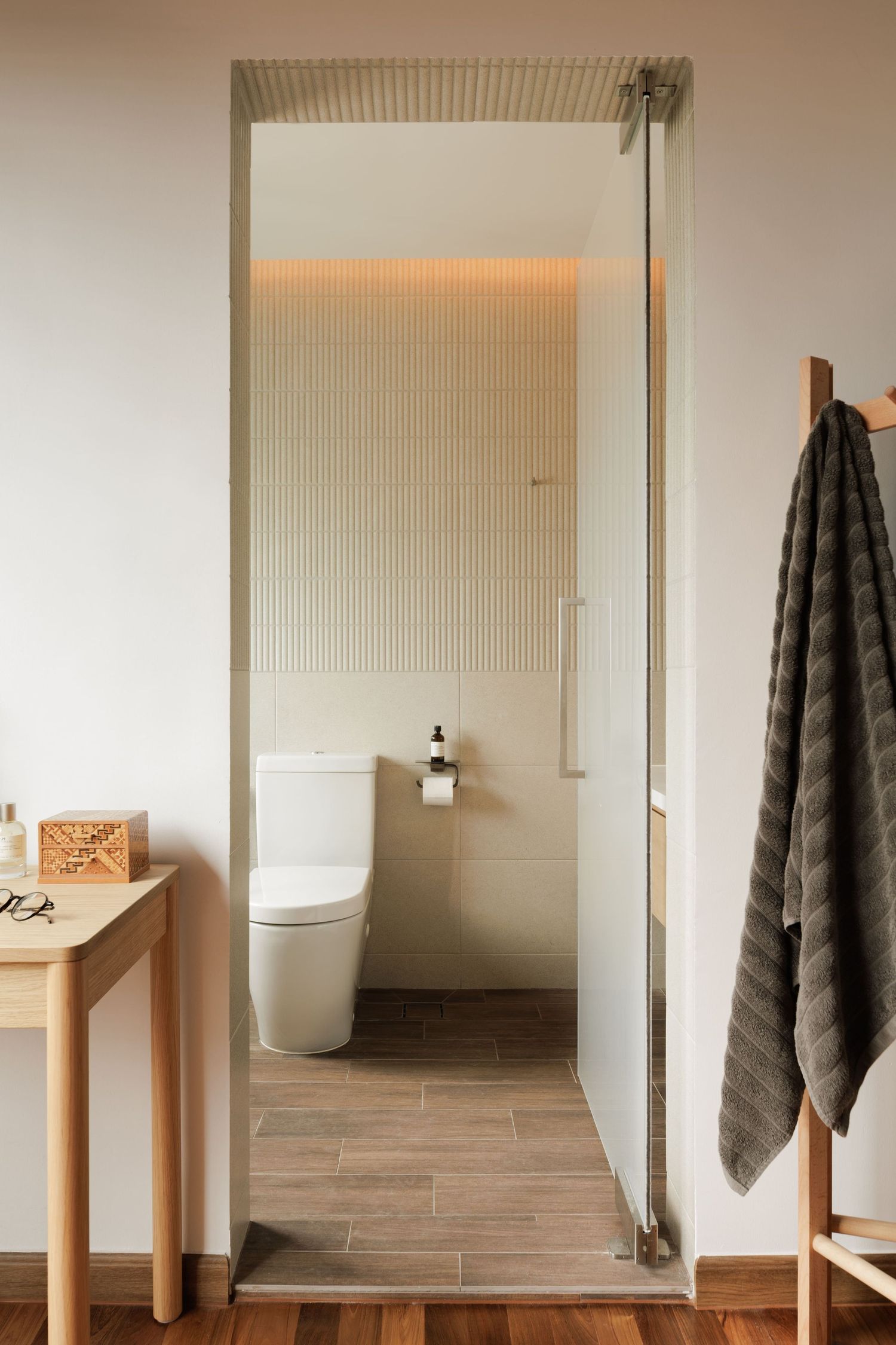 Minimalist bathroom interior with light wood pedestal sink, gray towel, and beige tiled floor in modern design.