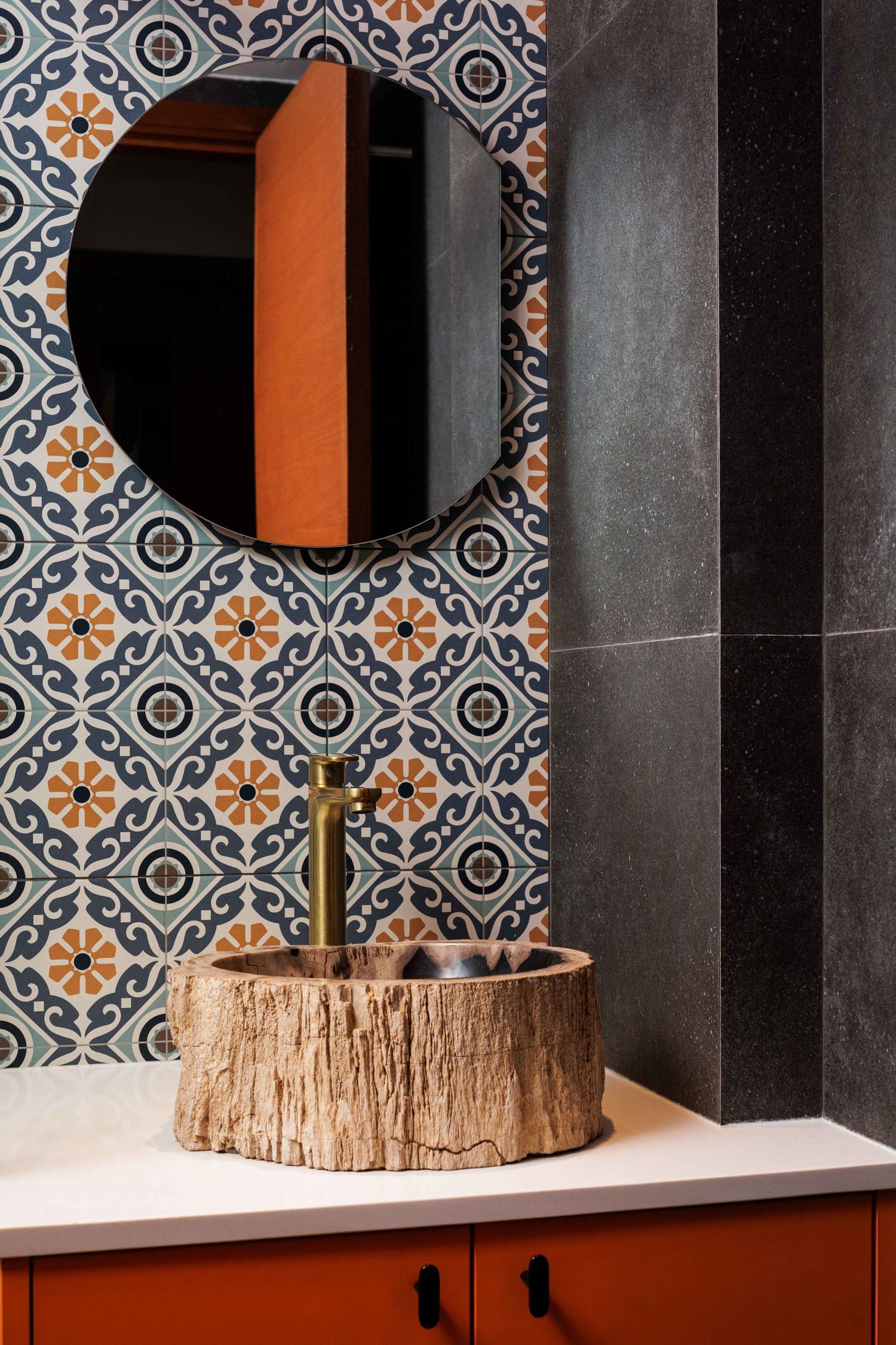 Modern bathroom with geometric patterned wallpaper, round mirror, and rustic wood vessel sink on orange cabinet.