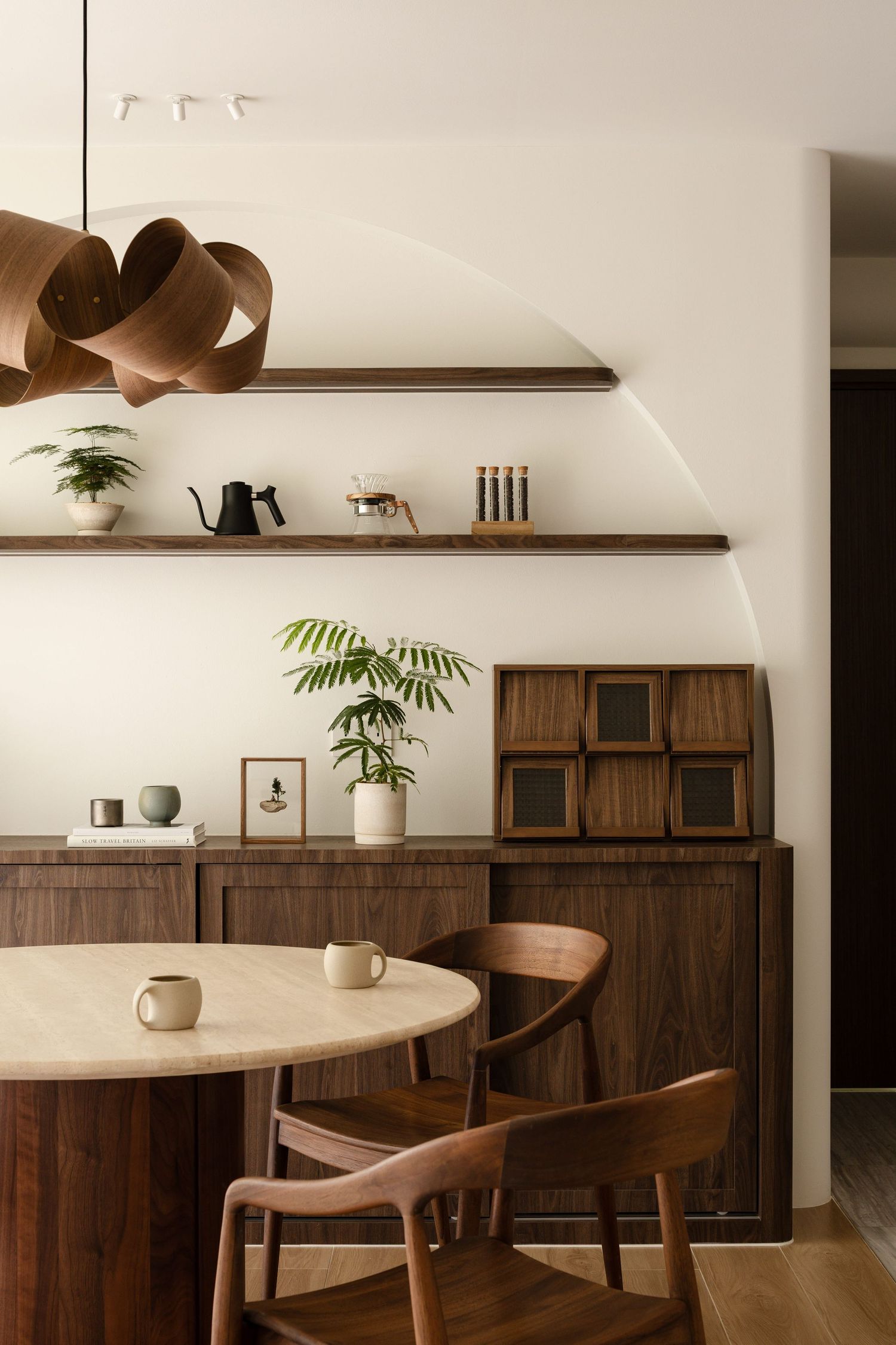 Modern dining space featuring dark wood cabinets, floating shelves, and round wooden table in a minimalist setting.
