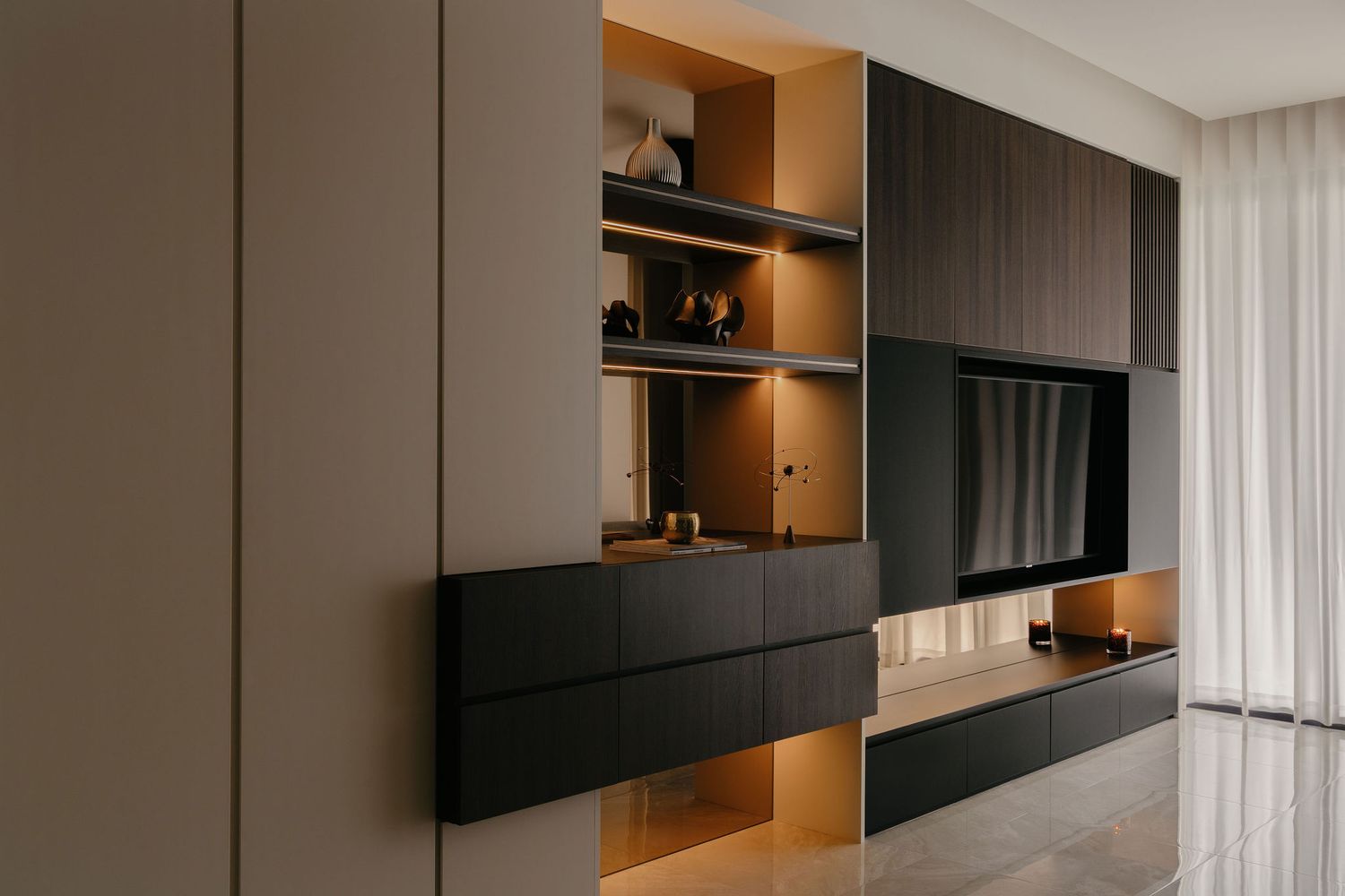 Modern living room with a dark wood built-in wall unit, wall-mounted TV, open shelving with warm LED lighting, and polished marble flooring.