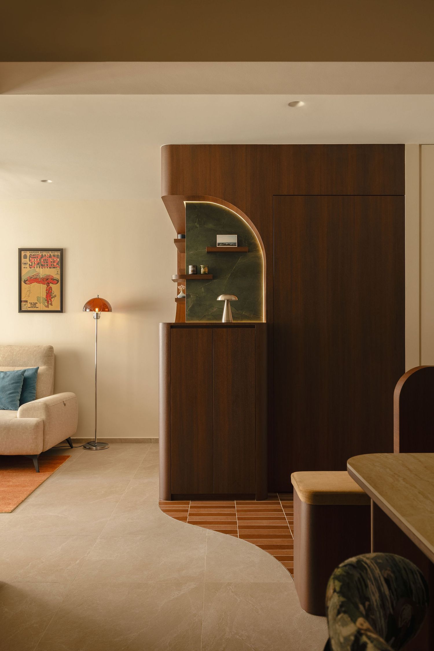 Modern living room with a walnut wood entry divider, green arched niche, curved tile floor transition, orange floor lamp and cream sofa.