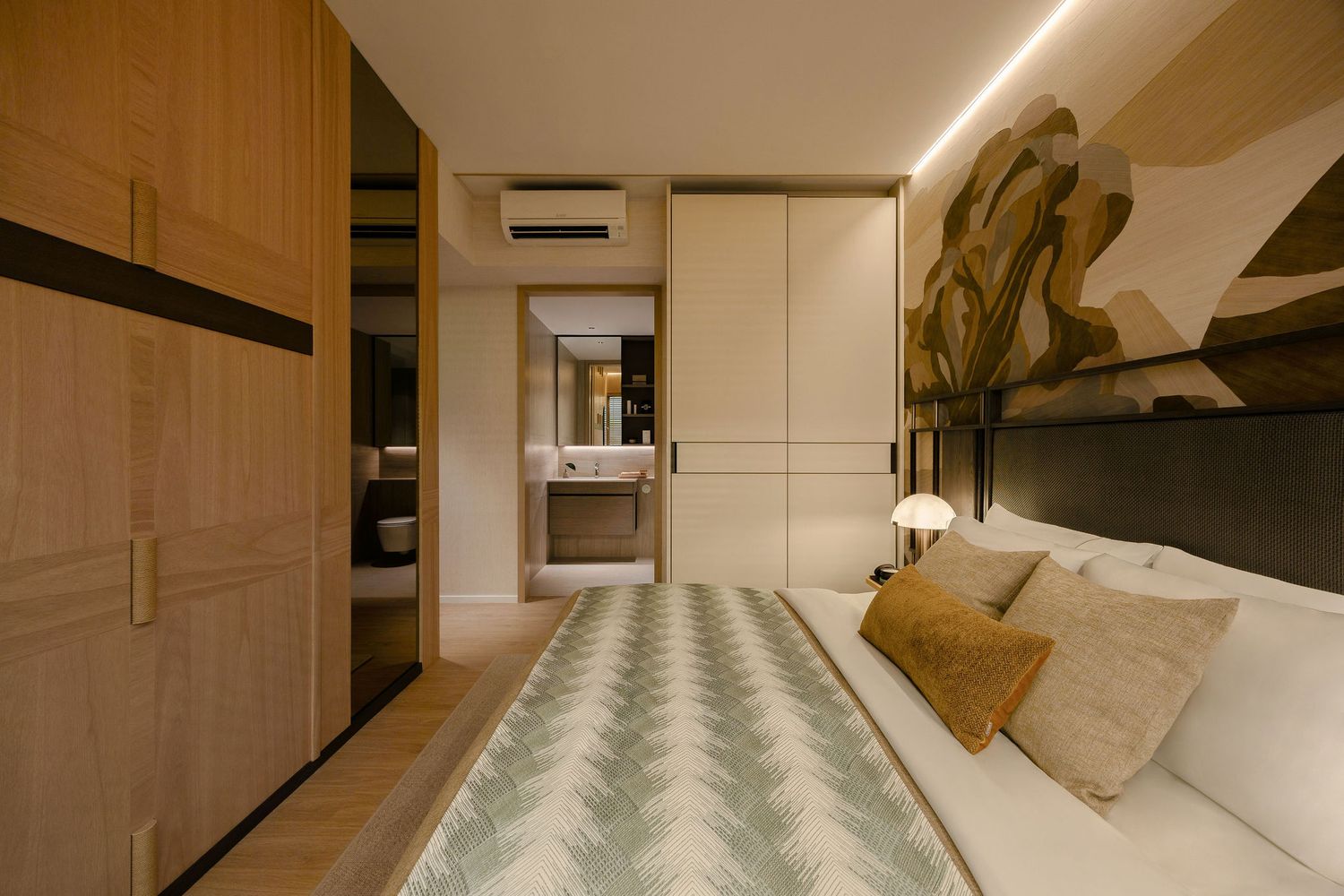 Modern bedroom with a white bed, chevron throw, tan cushions, wood panel wardrobe, abstract wall art, and a view into an ensuite bathroom.