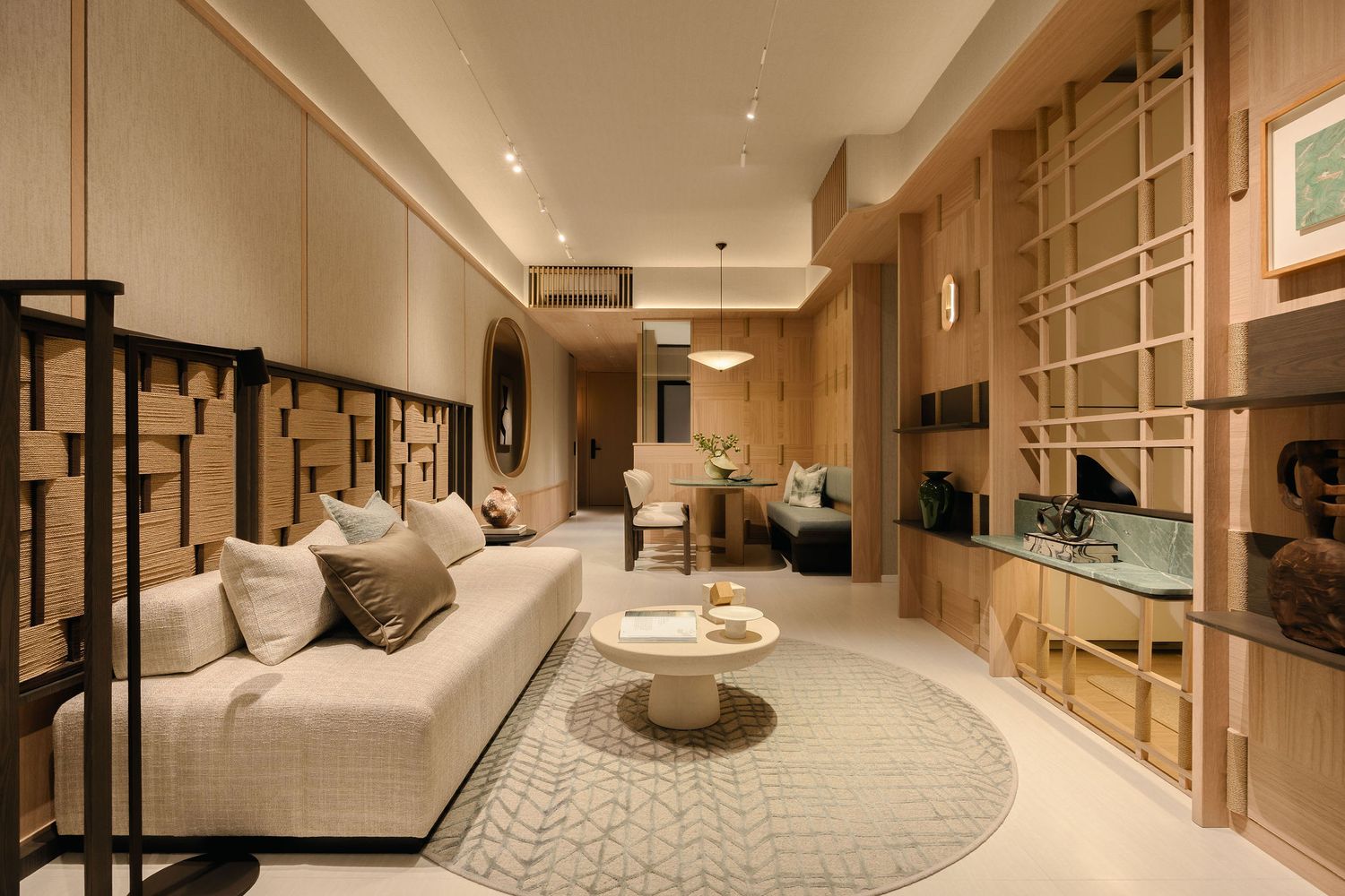 Modern living room with a cream sofa, round coffee table, patterned rug, and warm wood slat paneling in a bright, elegant apartment.
