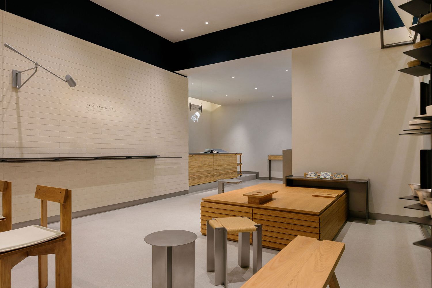 Modern minimalist cafe interior with light wood tables, stools, and chairs, a reception counter in the background, and clean beige walls.