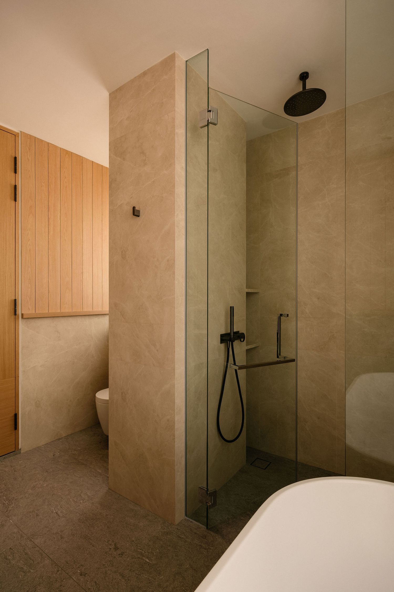 Modern bathroom with beige stone-look walls, a frameless glass shower with black fixtures, wood paneling, a wall-hung toilet and a freestand
