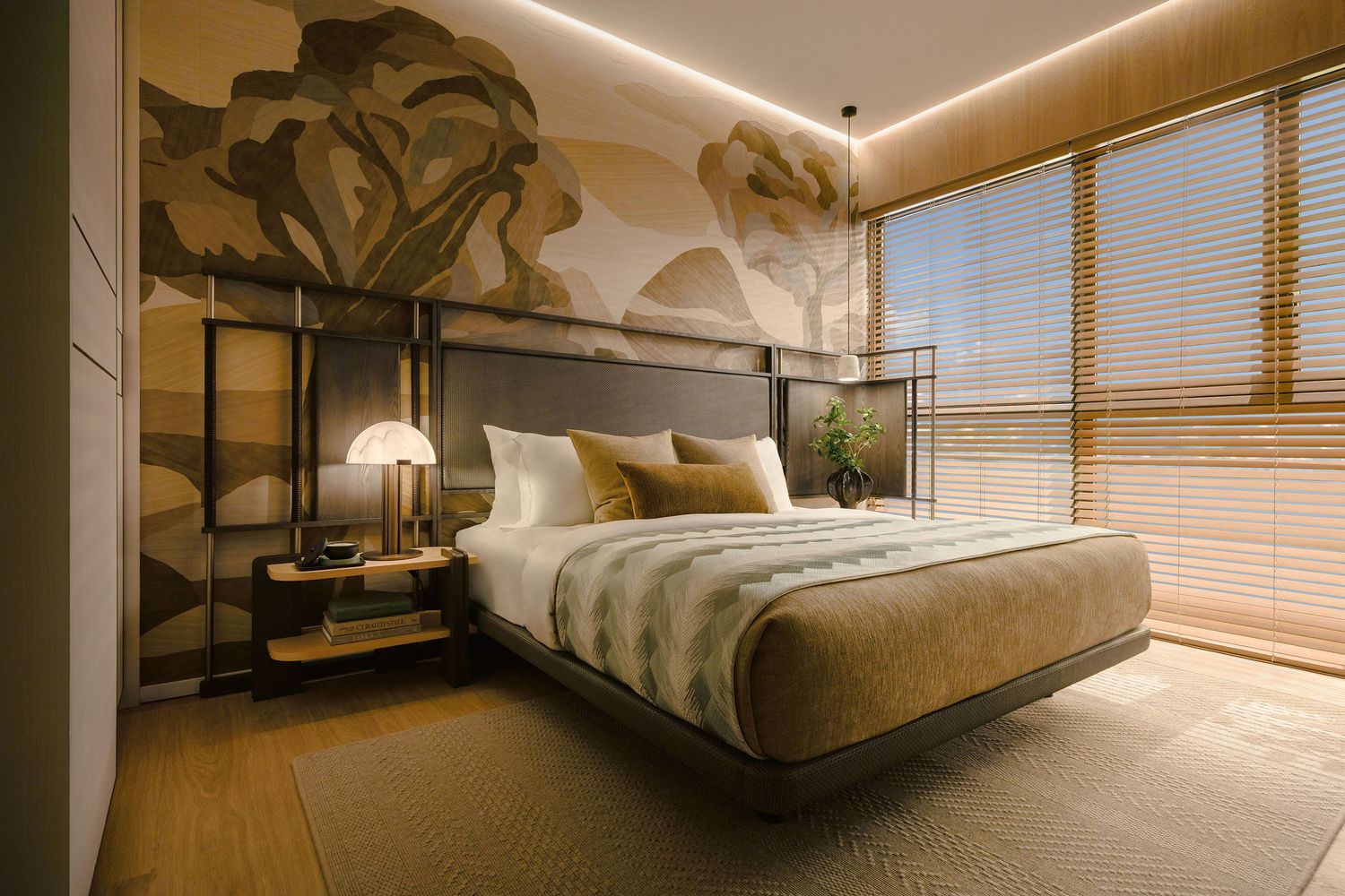 Modern bedroom with a low platform bed, tan bedding, botanical mural wall, warm wood flooring, bedside lamp and shuttered window blinds.