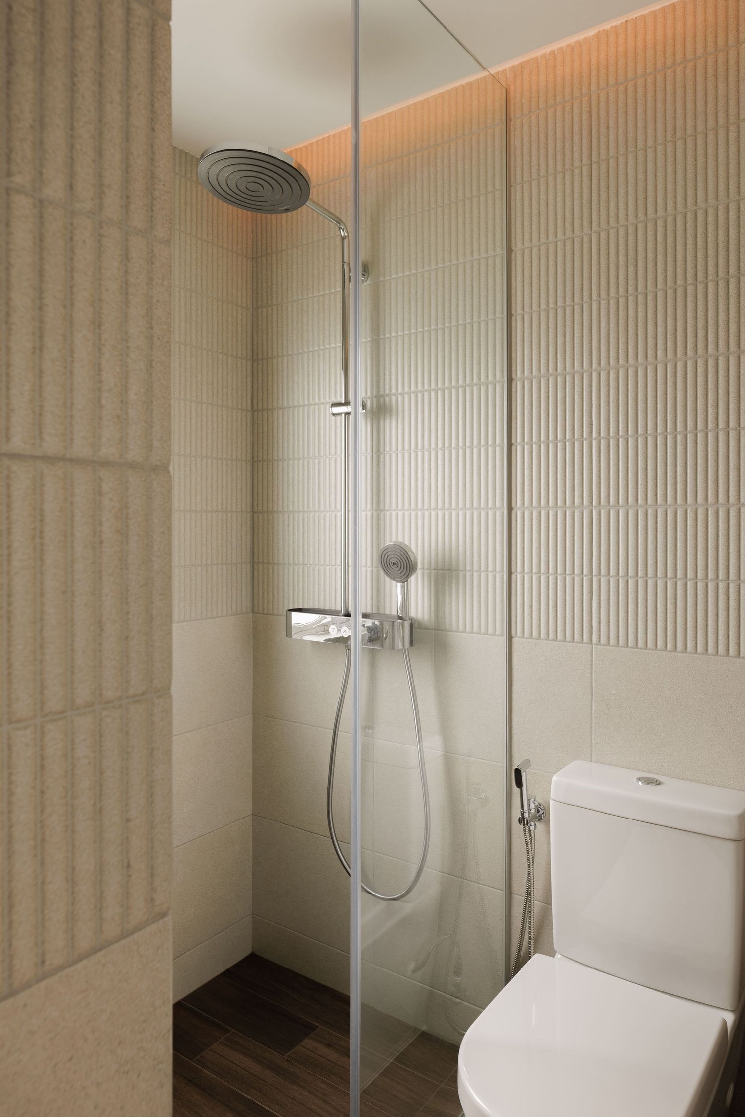 Modern bathroom interior with beige textured walls, glass shower enclosure, and white porcelain fixtures.